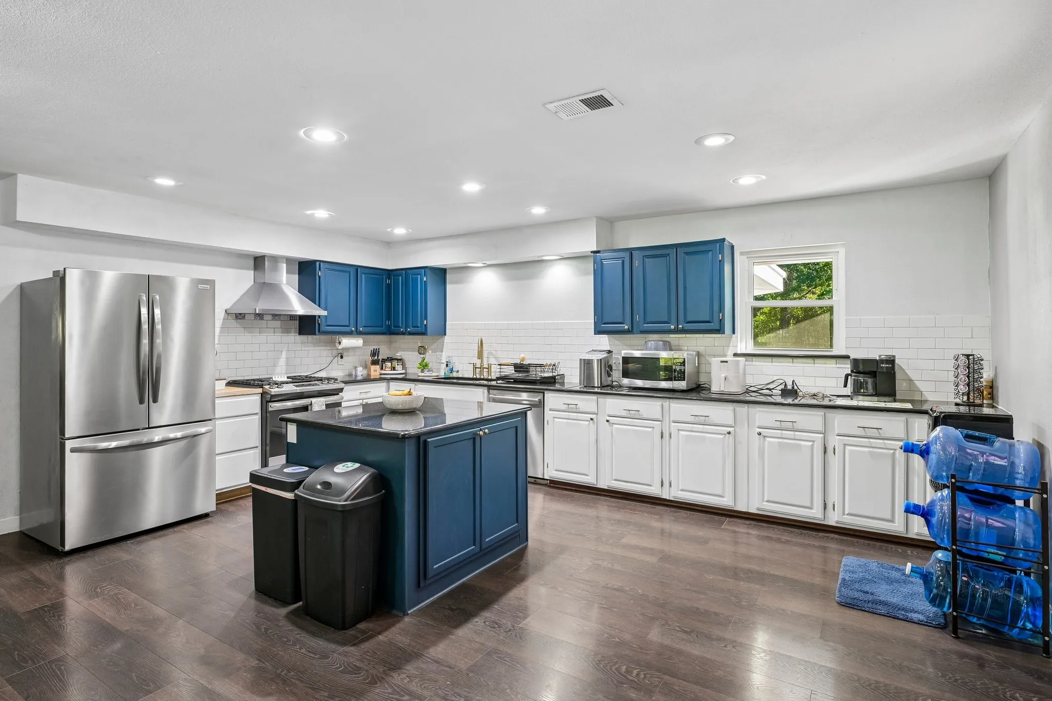 Kitchen featuring dark wood-finish flooring, a central island with a dark countertop, white subway tile backsplash, recessed lighting, and stainless steel appliances