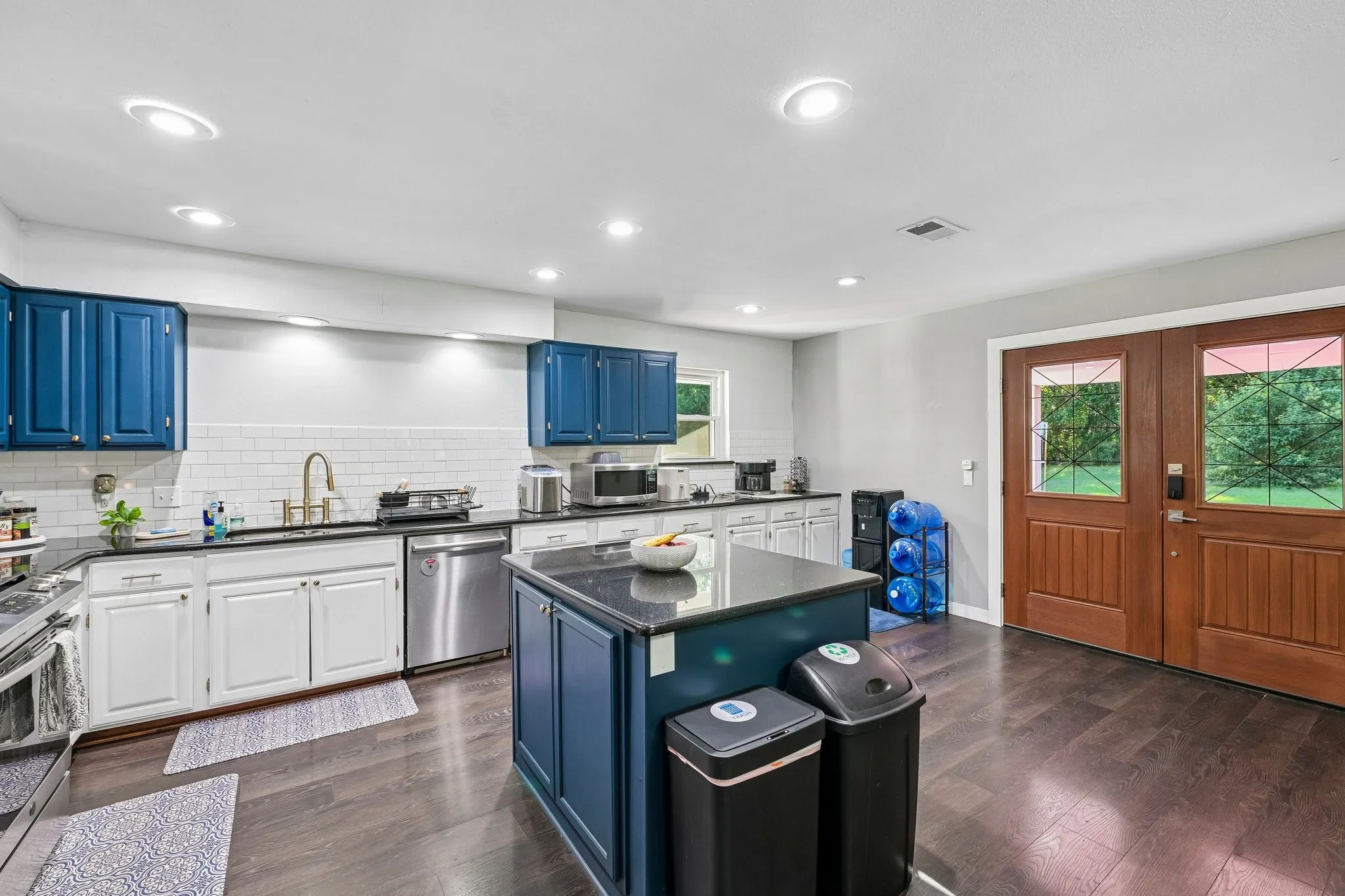 Kitchen featuring an island with stone countertop, stainless steel dishwasher, white subway tile backsplash, recessed lighting, and wood-finish flooring