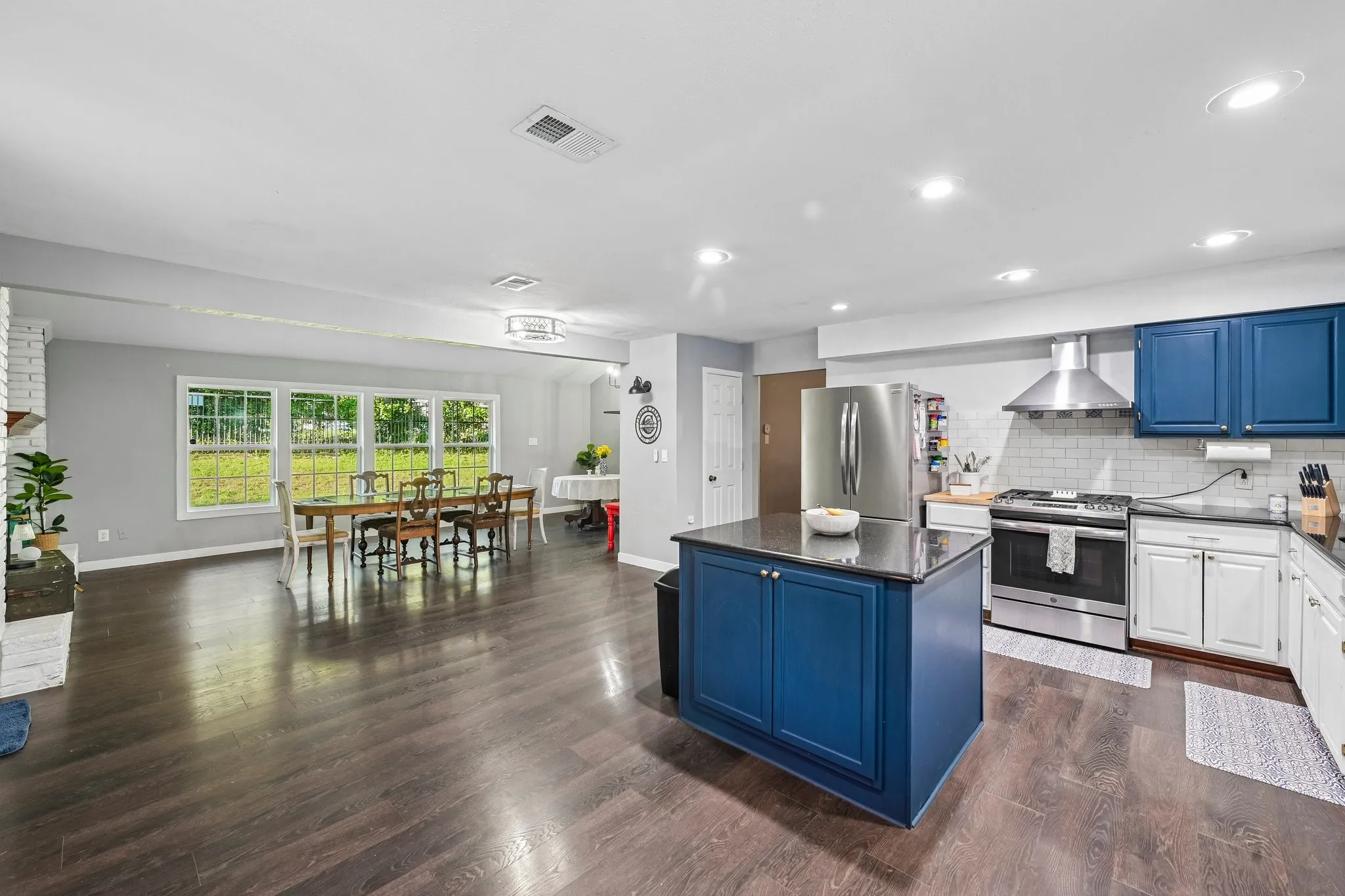 Open-concept living area featuring wood-finish flooring, a kitchen island with storage, stainless steel appliances, and large windows