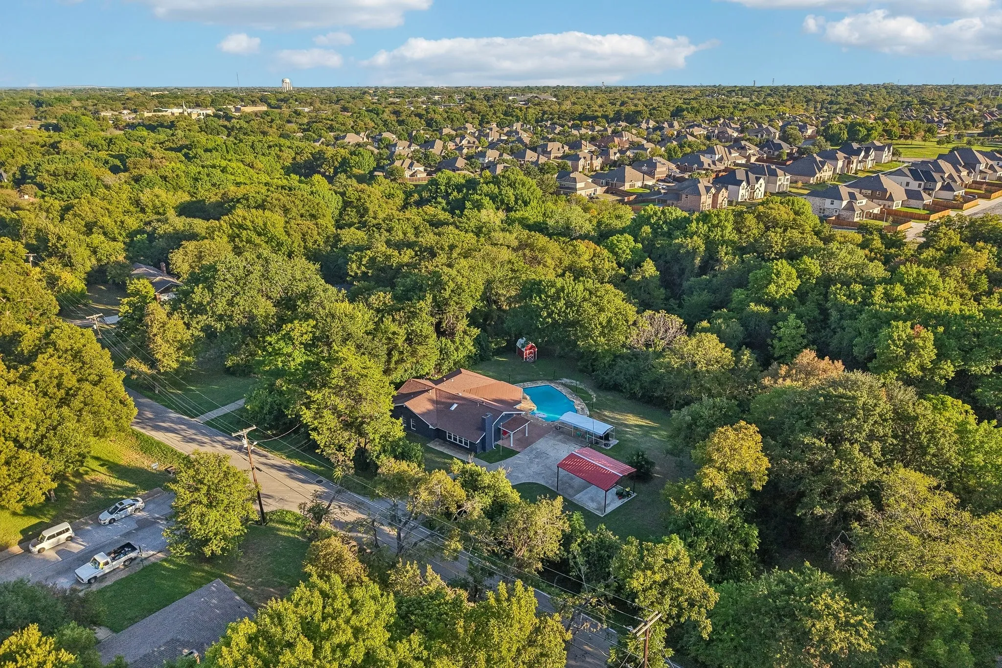 Residence featuring a private swimming pool, extensive tree canopy, and a detached carport structure
