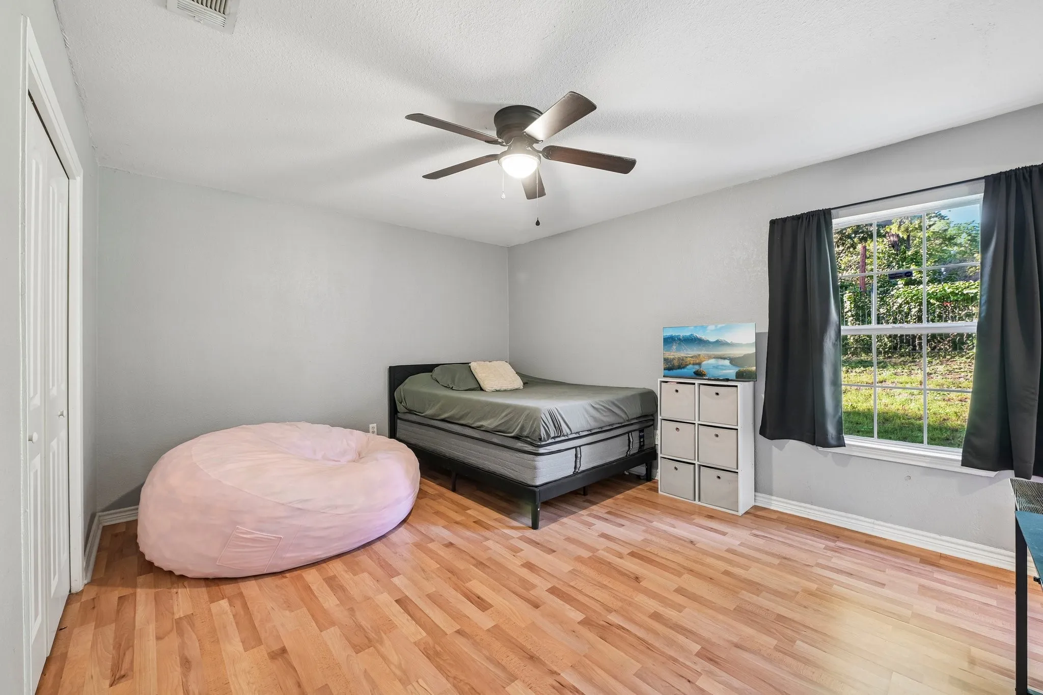 Wood-finish flooring, ceiling fan, white bi-fold closet doors, and a window with a natural outdoor backdrop