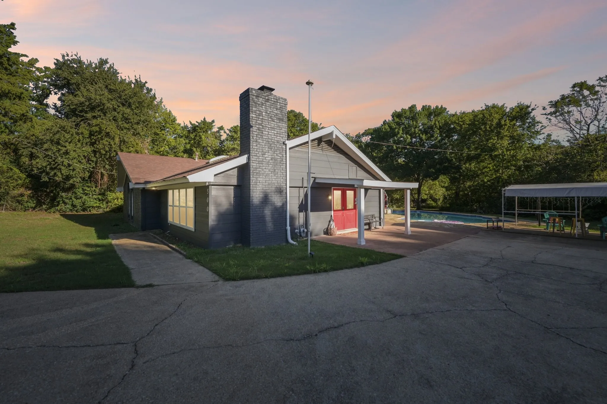 Exterior featuring a grey siding finish, dark brick chimney, covered patio, and an in-ground pool