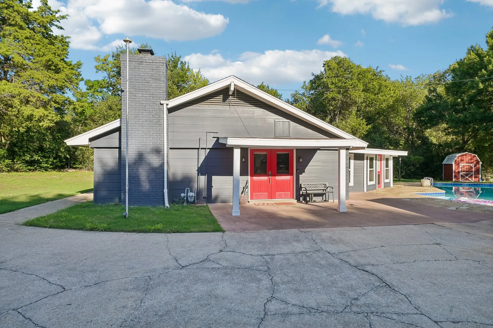 Exterior featuring gray horizontal siding, a prominent brick chimney, red double entry doors, a covered patio, and an adjacent swimming pool