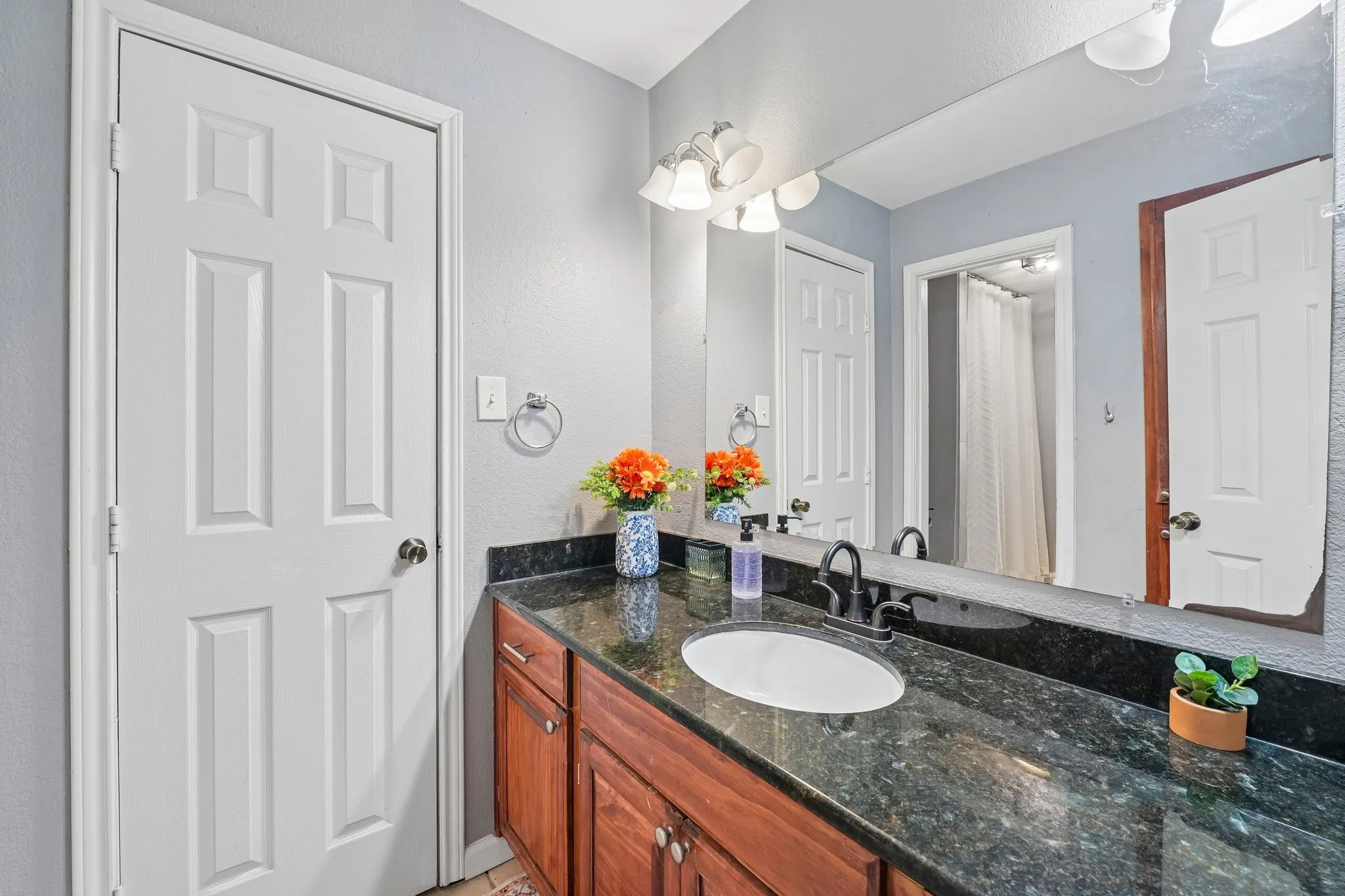 Vanity with dark granite countertop, undermount sink, dark bronze faucet, and wood-finish cabinetry