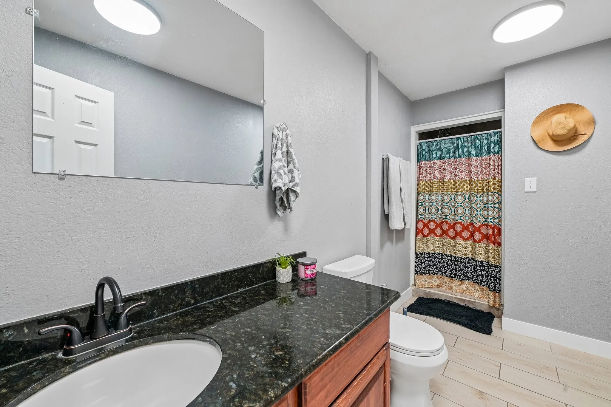 Wood-finish vanity with an undermount sink, dark speckled countertop, and wall-mounted mirror