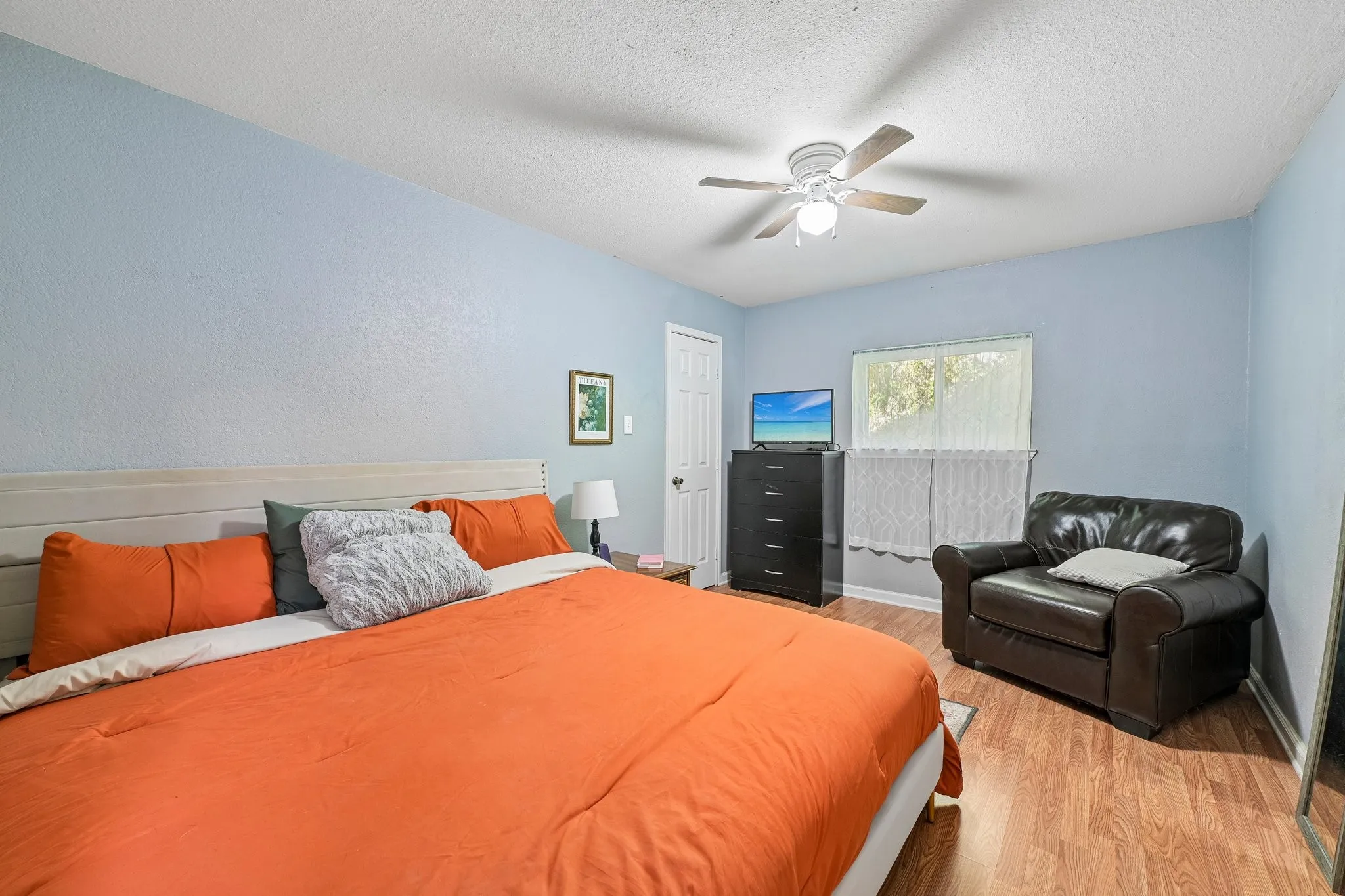 Ceiling fan with integrated lighting, wood-finish flooring, and a window providing natural illumination