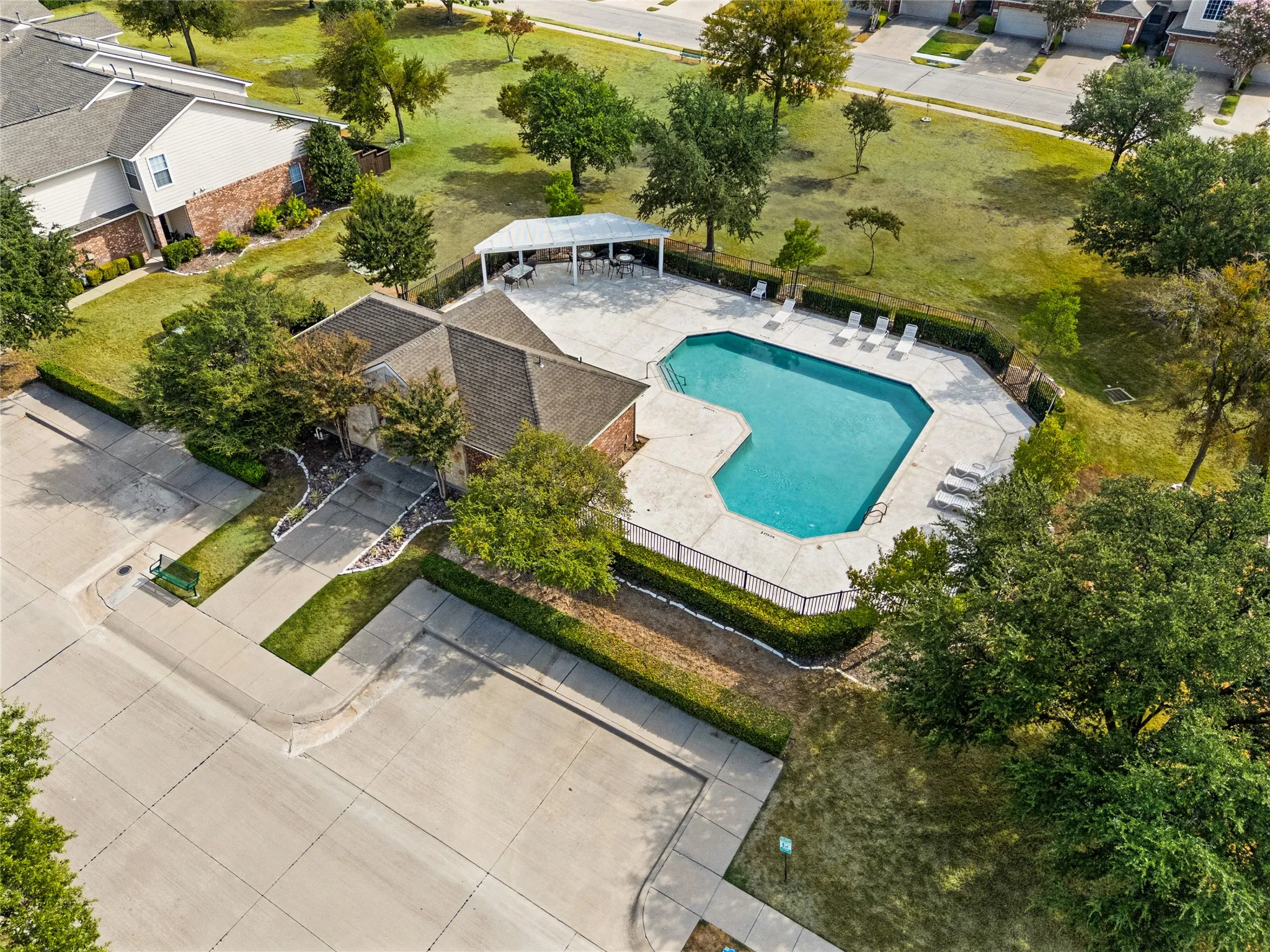 Geometric-shaped pool with concrete decking, surrounding privacy fencing, and an adjacent covered cabana area