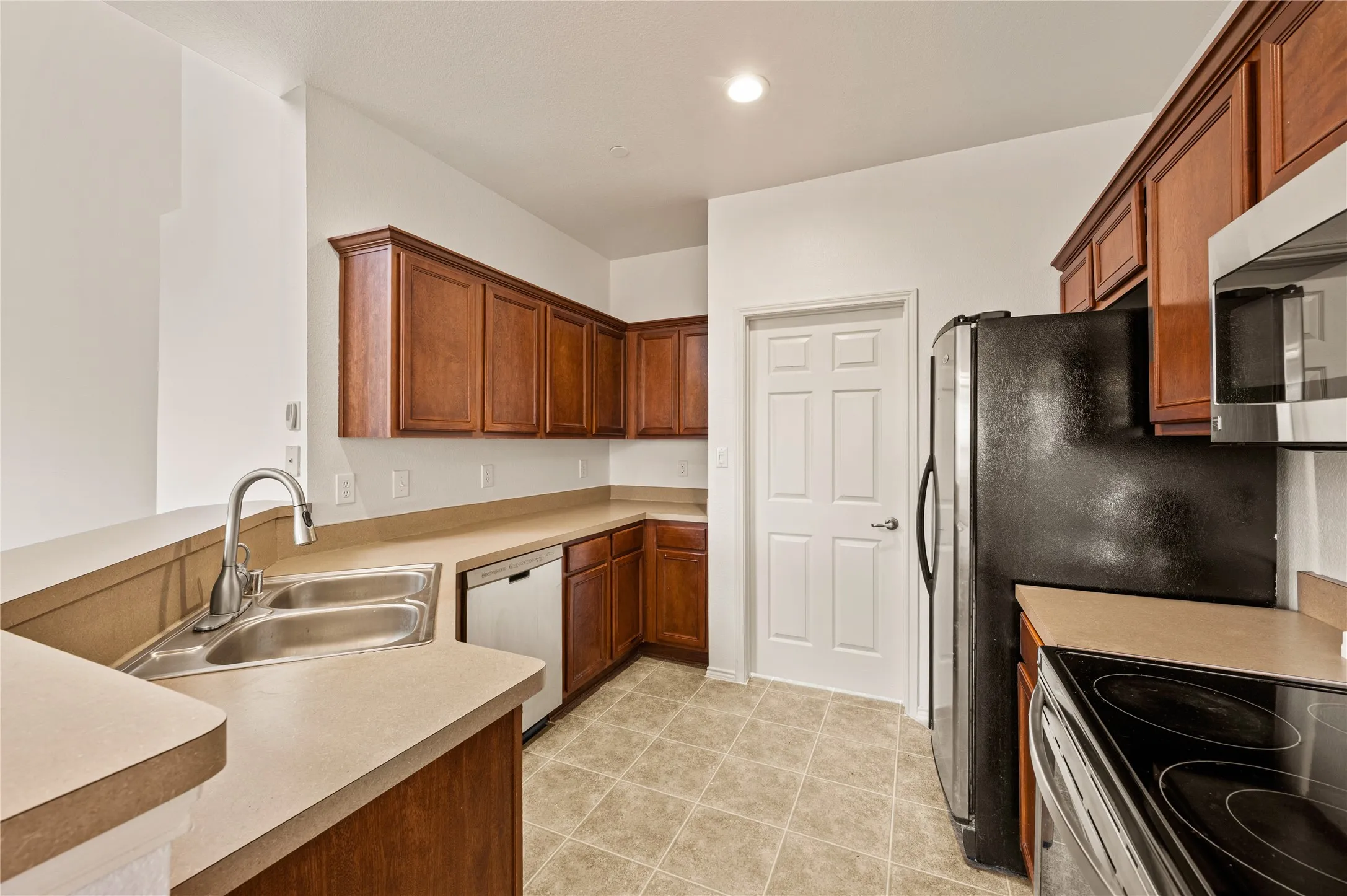 Kitchen featuring wood-finish cabinetry, solid surface countertops, a stainless steel double-basin sink with a gooseneck faucet, a built-in dishwasher, and tile flooring