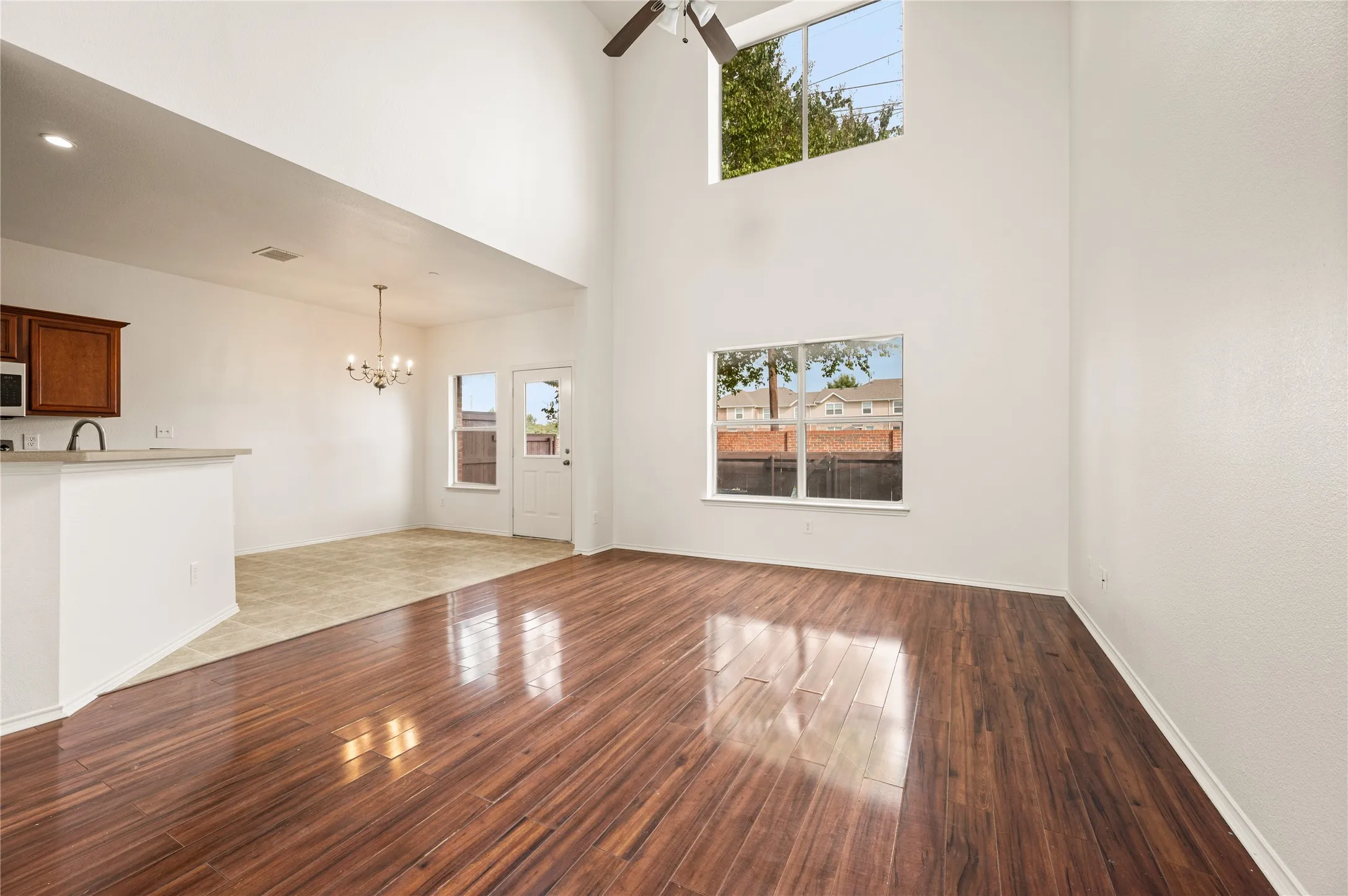 Soaring ceilings with a high-mounted window, wood-finish flooring, a contemporary ceiling fan, and an open-concept layout to the dining area featuring a chandelier