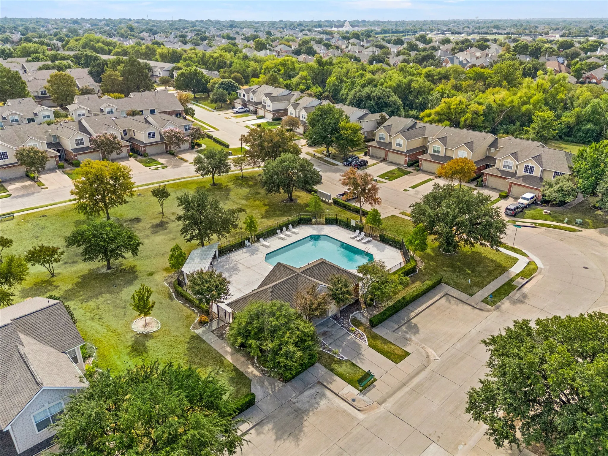 Community pool with surrounding patio, mature trees, and landscaping