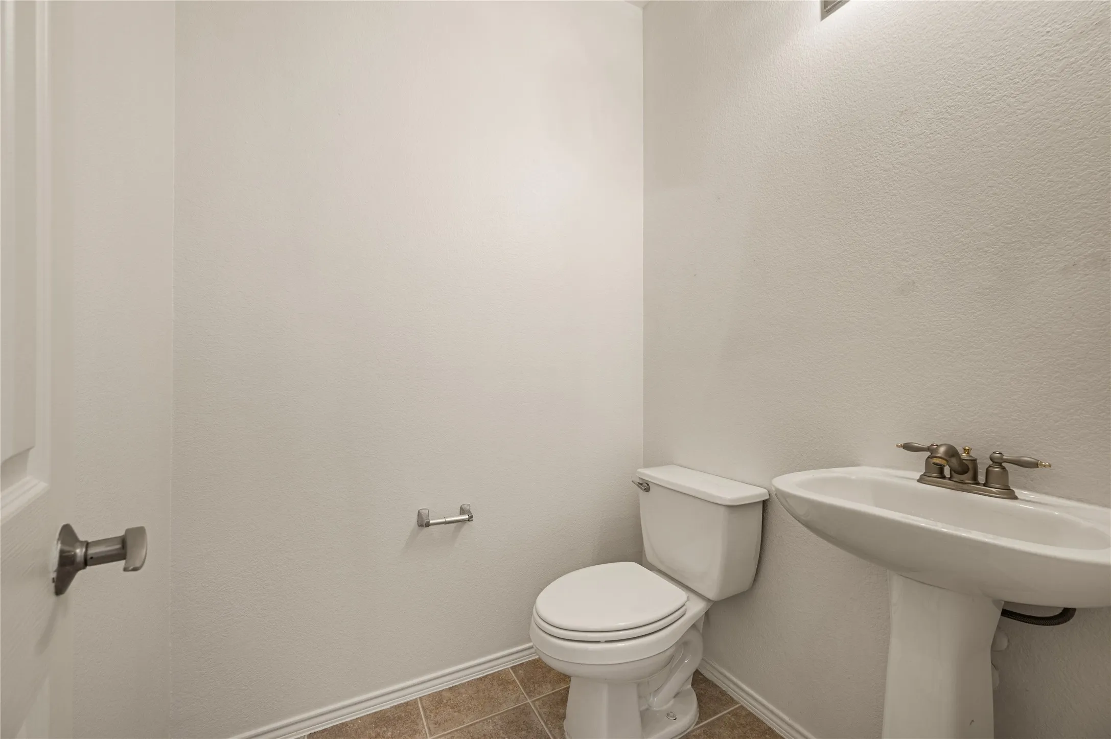Pedestal sink with a two-handle faucet, white toilet, and tiled flooring