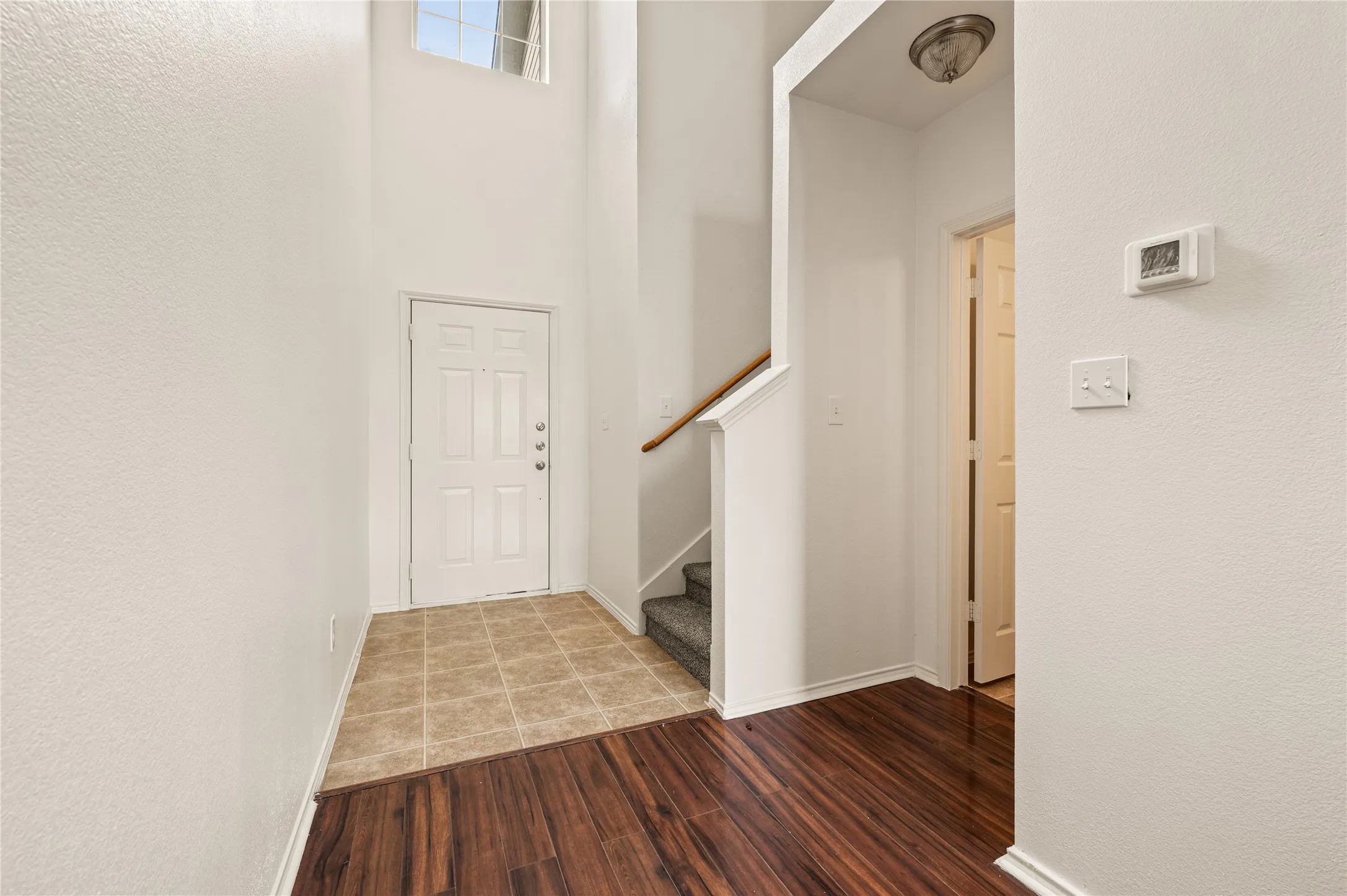 Two-story foyer with a transom window, wood-finish flooring, and a tiled entry
