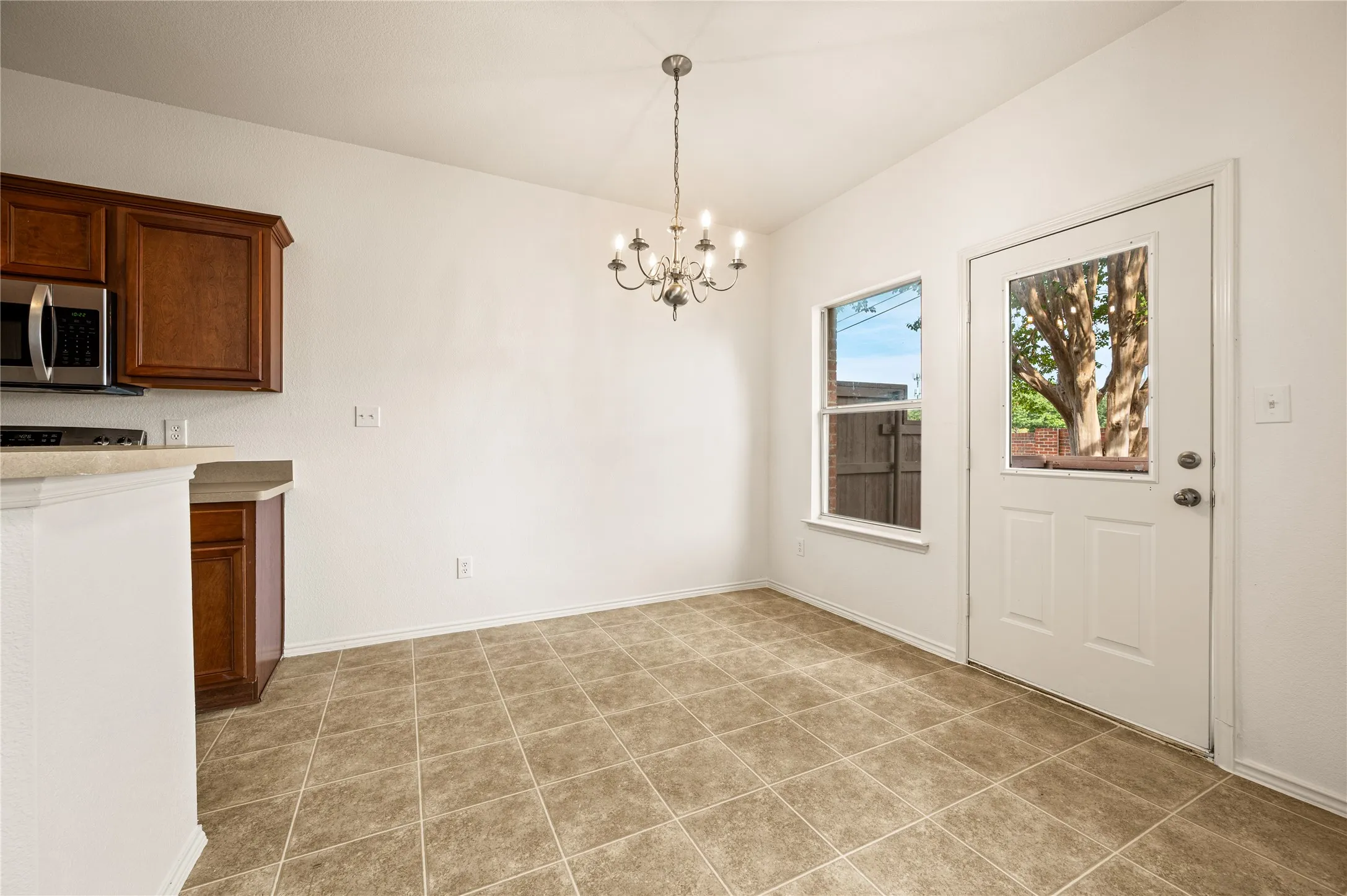Vaulted ceiling with chandelier lighting, tile flooring, wood-finish cabinetry, stainless steel microwave, and exterior door with integrated window