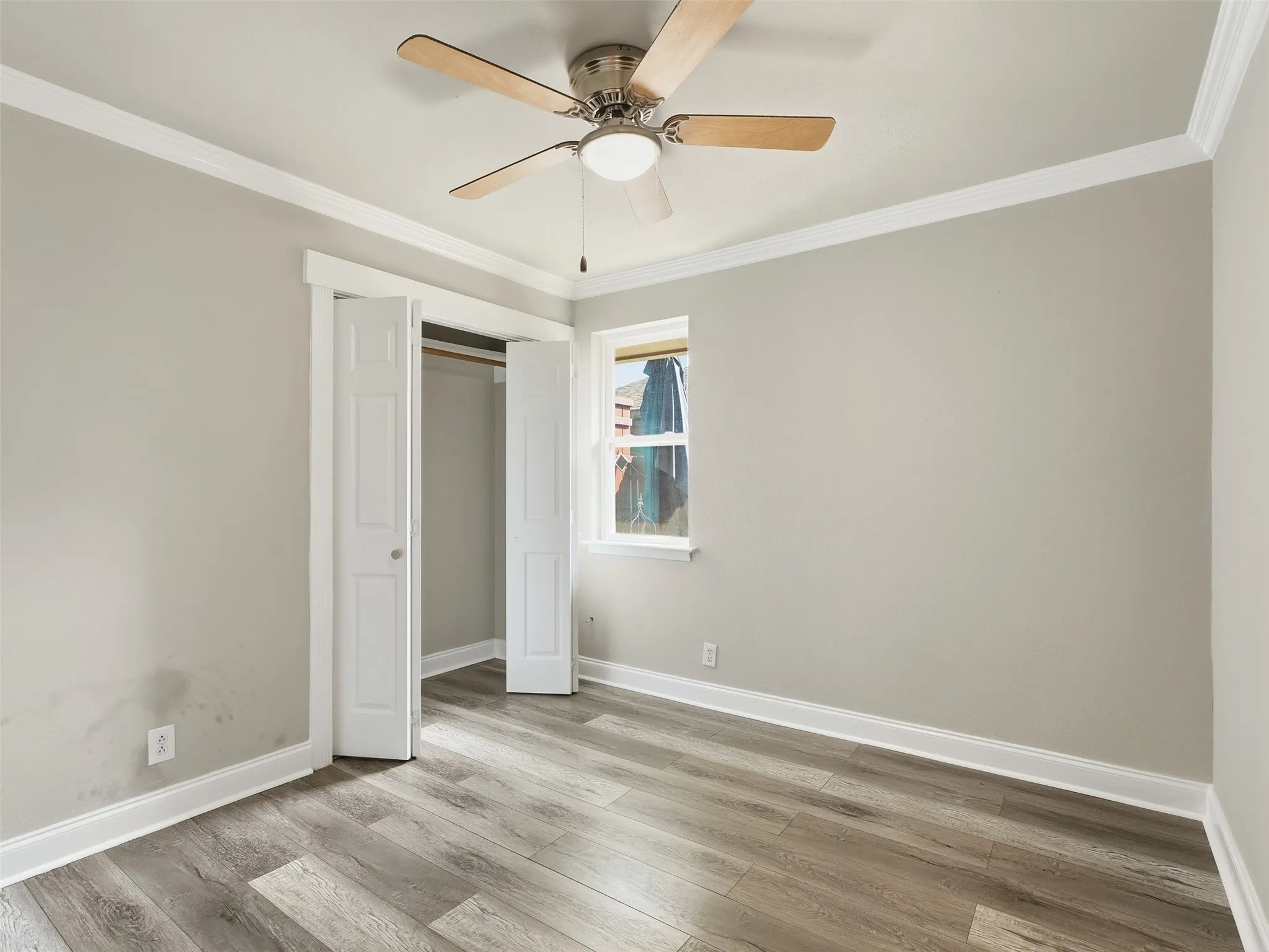 Wood-finish flooring, crown molding, ceiling fan with integrated lighting, and a double-door closet