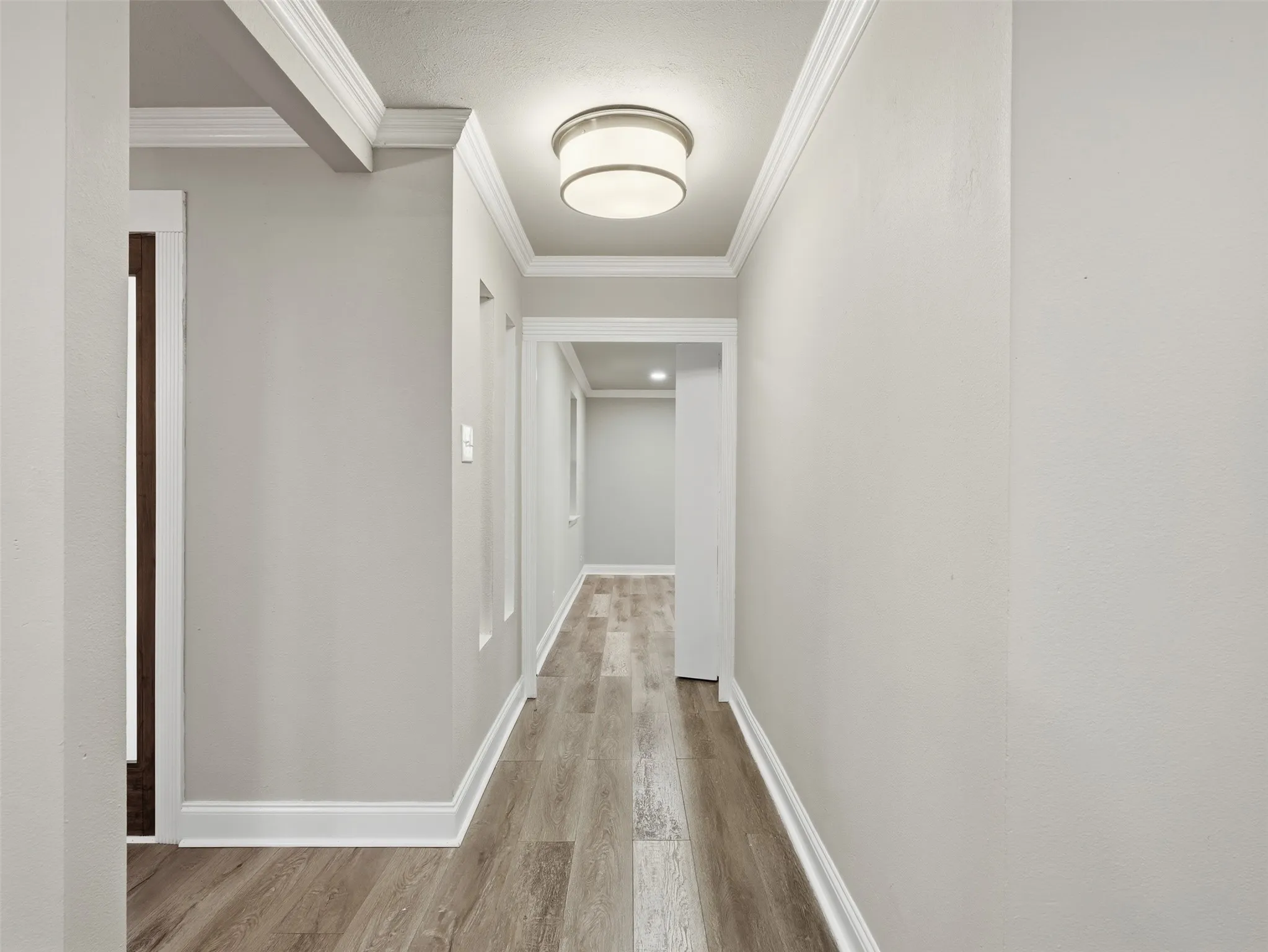 Hallway with wood-finish flooring, crown molding, and a drum ceiling light fixture
