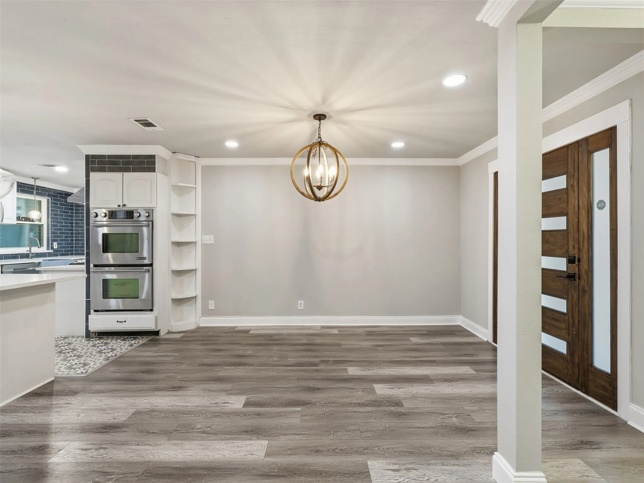 Wood-finish flooring, recessed lighting, and a modern orb chandelier illuminate this open space