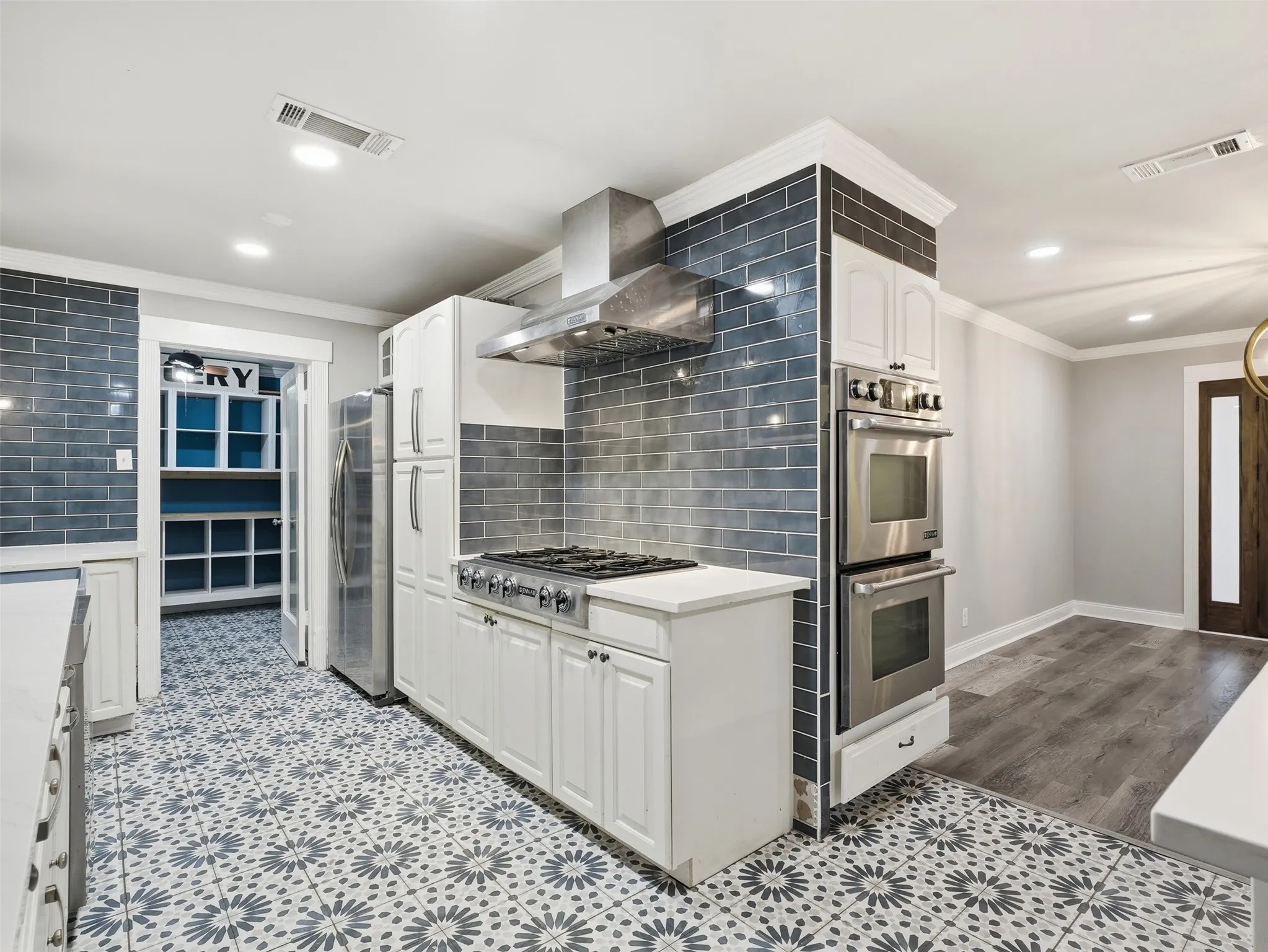 Gourmet kitchen featuring stainless steel appliances, a gas range, double wall ovens, a tile backsplash, and patterned tile flooring