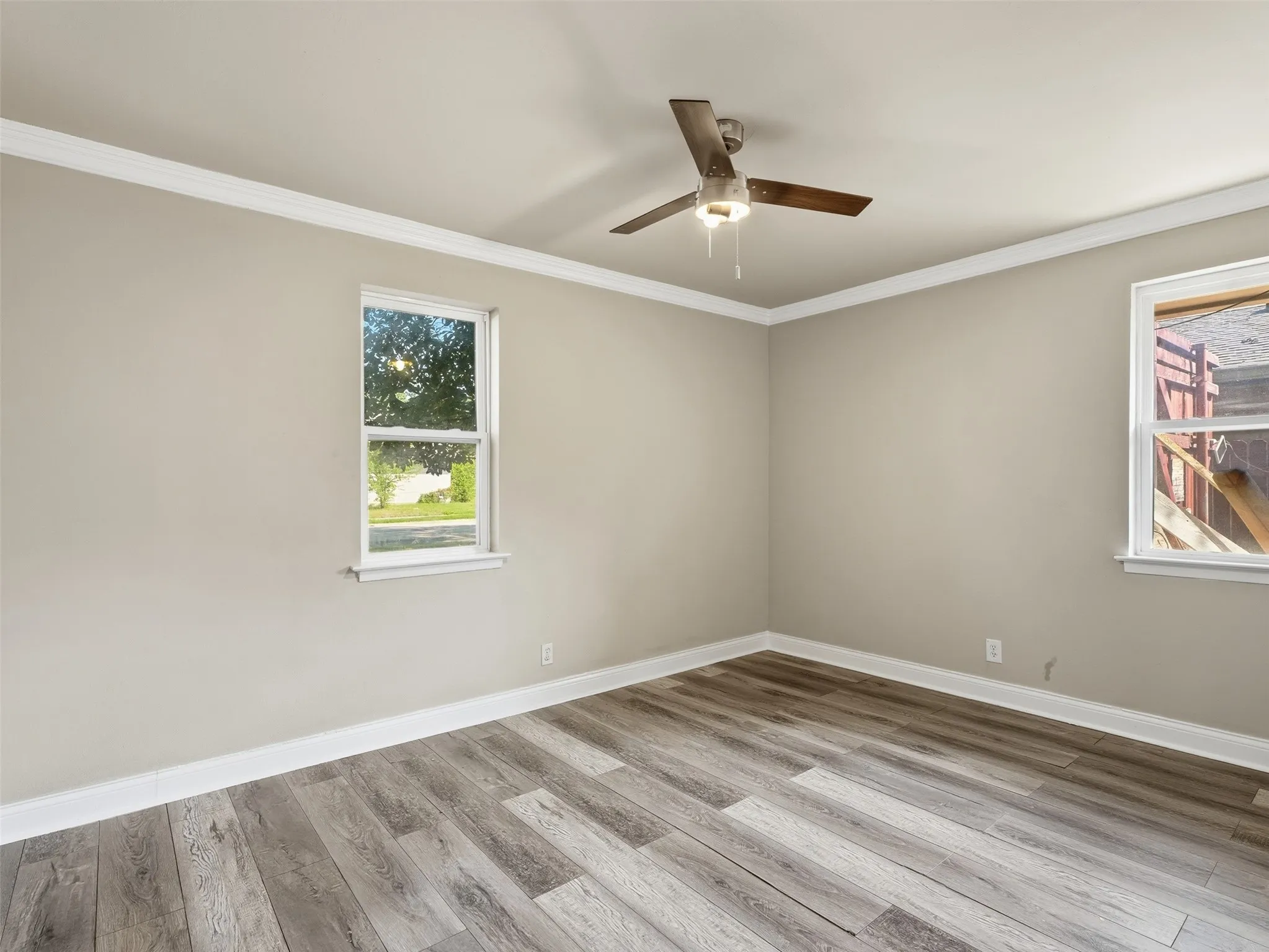 Wood-finish flooring, neutral wall tones, two windows with white trim, white crown molding, and a ceiling fan with light fixture