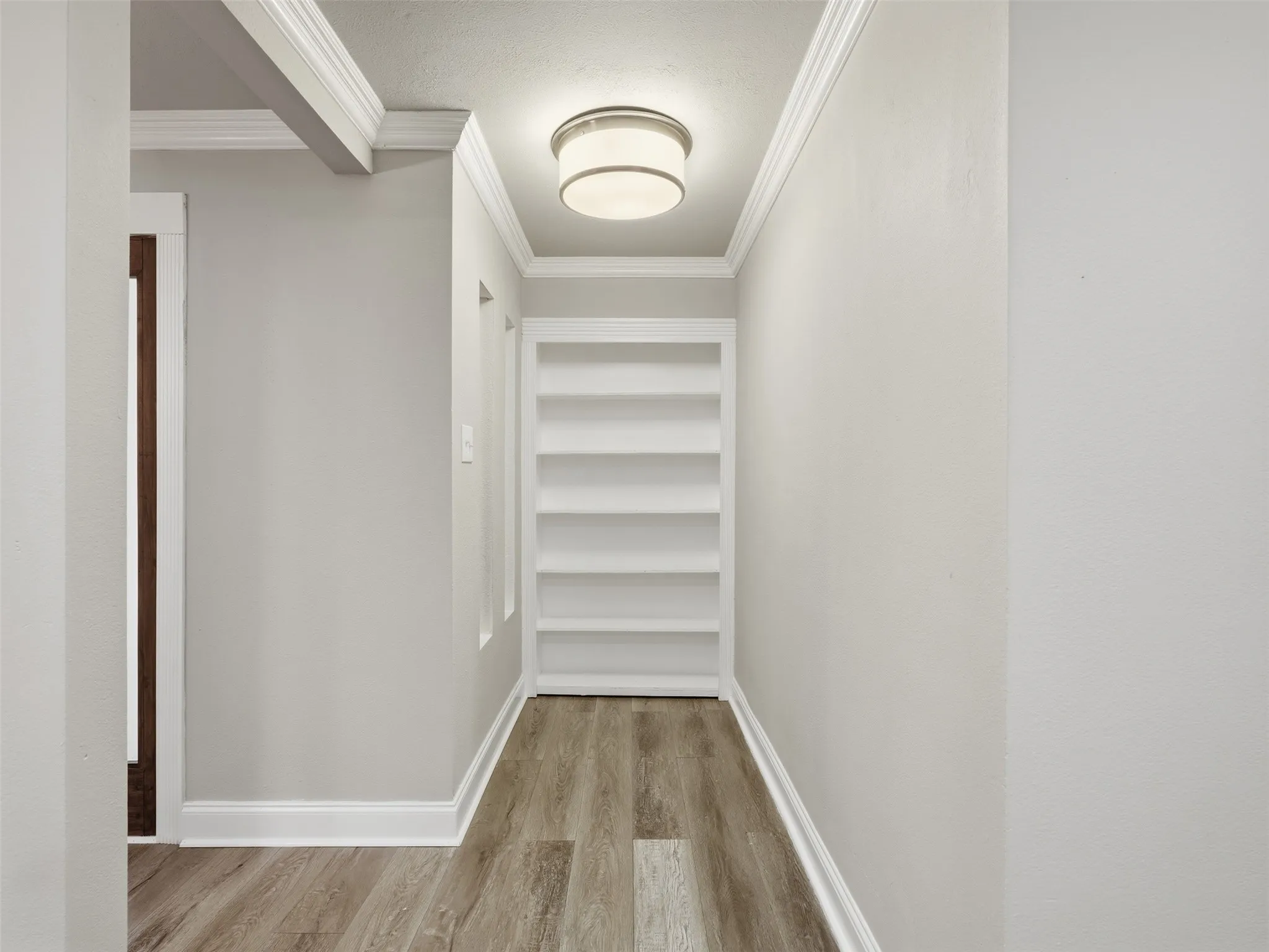 Hallway featuring built-in shelving, wood-finish flooring, recessed lighting, and crown molding