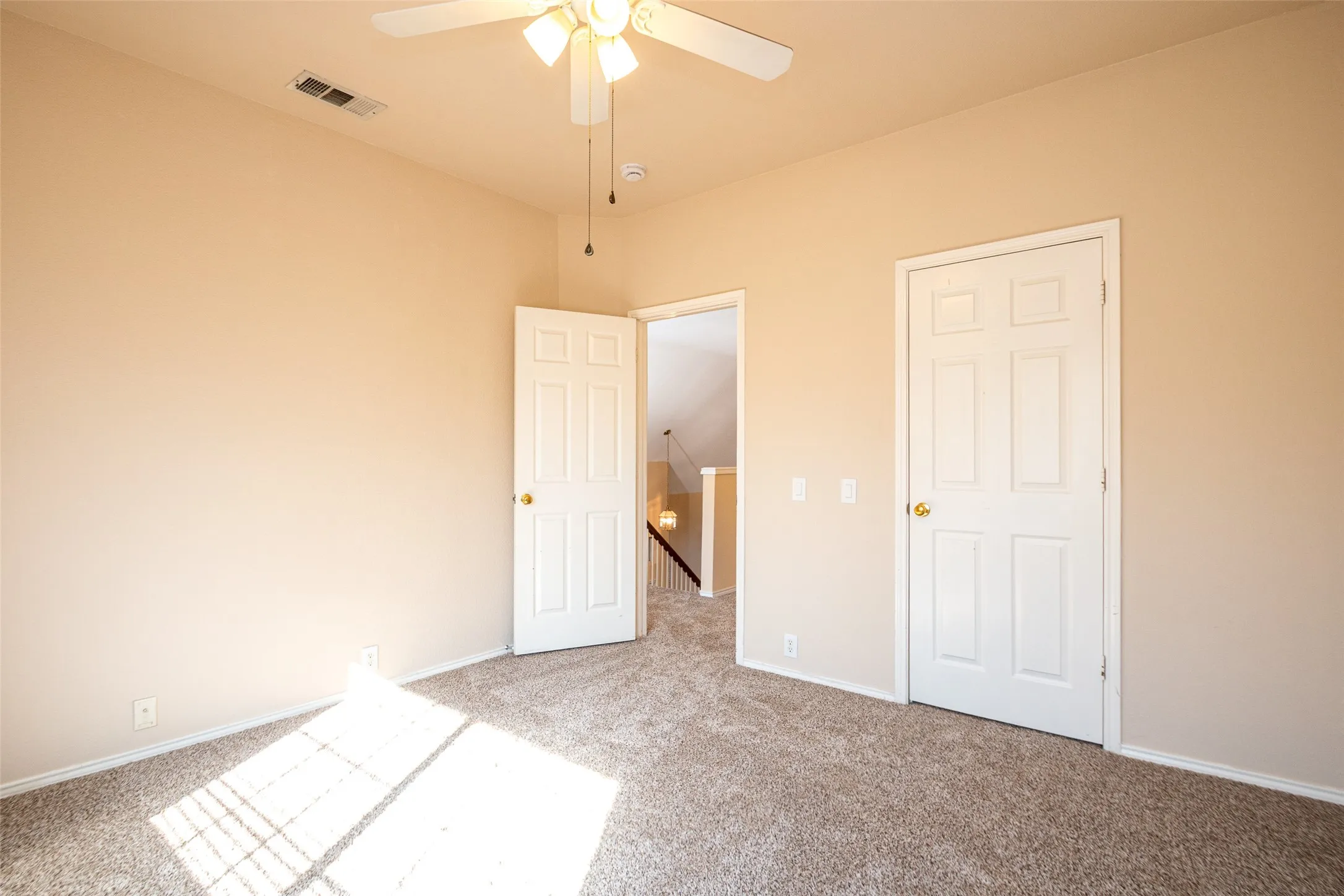 Textured carpeting, light neutral wall paint, overhead ceiling fan with lighting, white interior doors, and white trim throughout