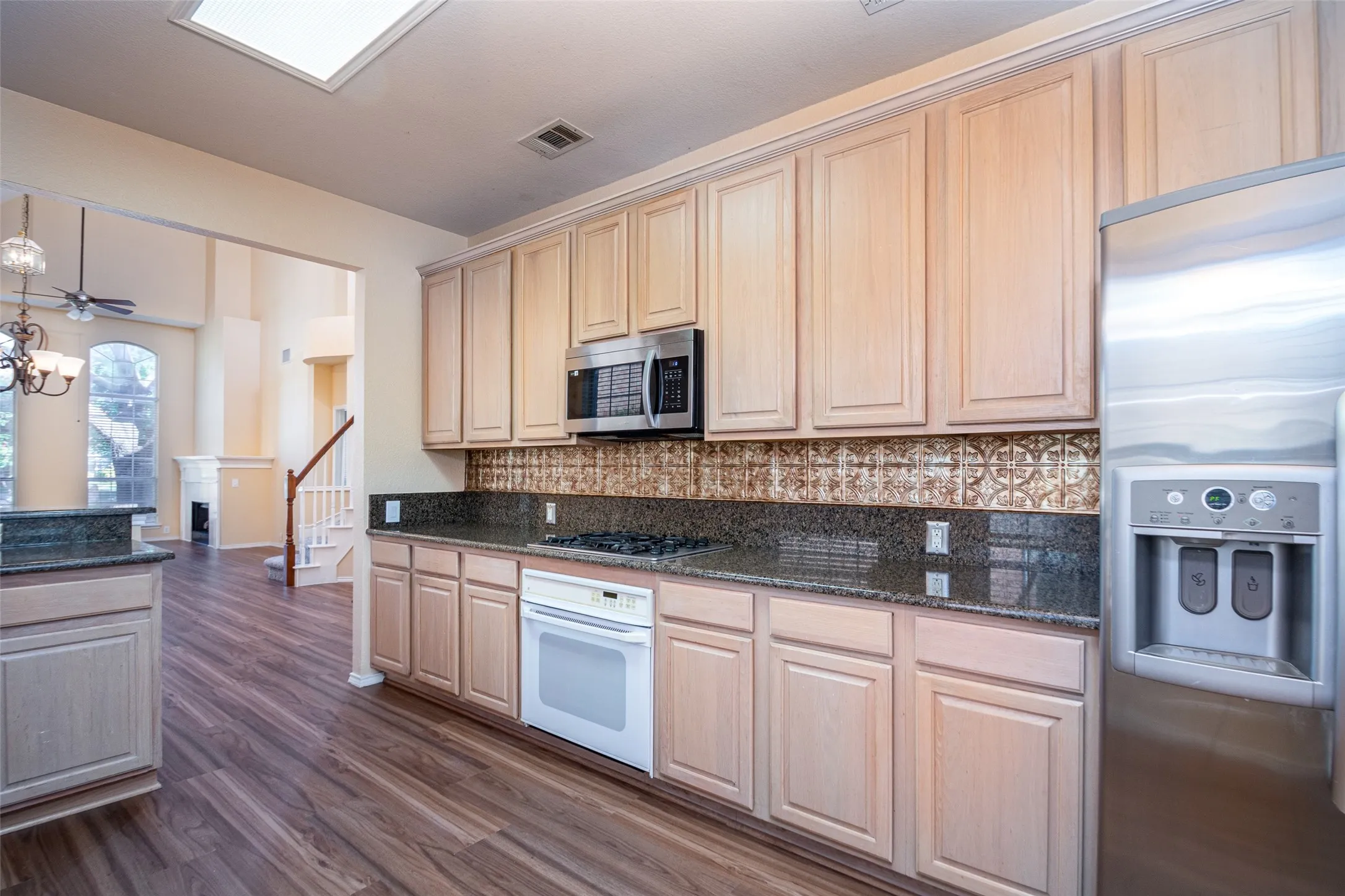 Kitchen featuring wood-finish flooring, dark stone countertops, light wood-finish cabinetry, and stainless steel appliances