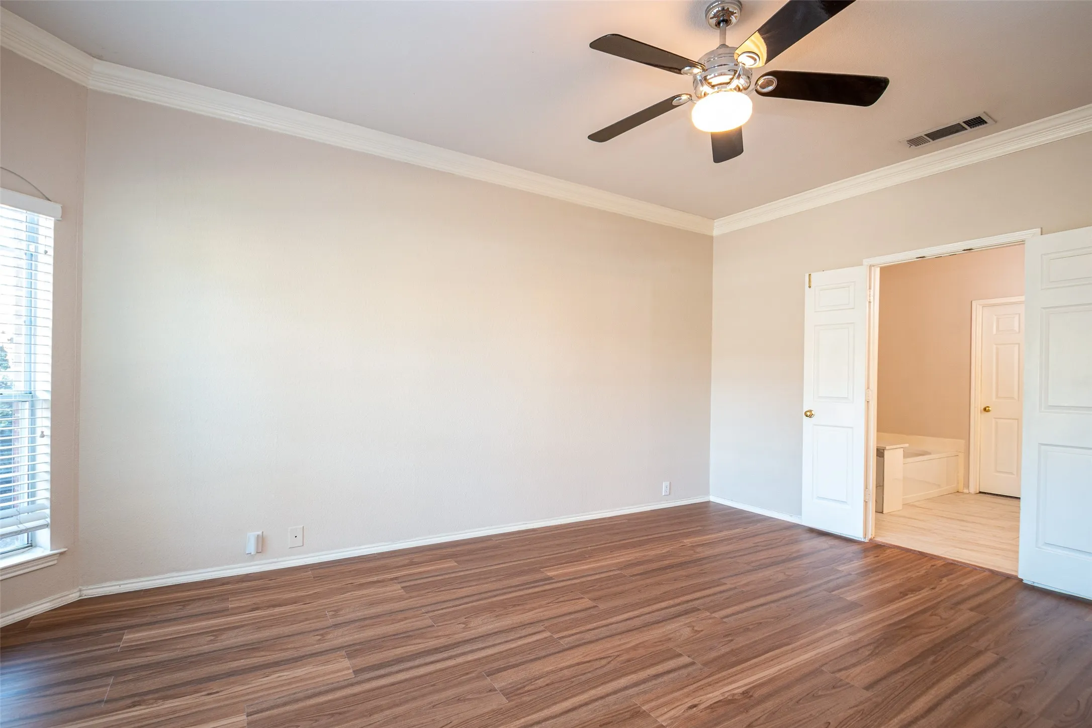 Spacious room with wood-finish flooring, crown molding, a ceiling fan, and double doors