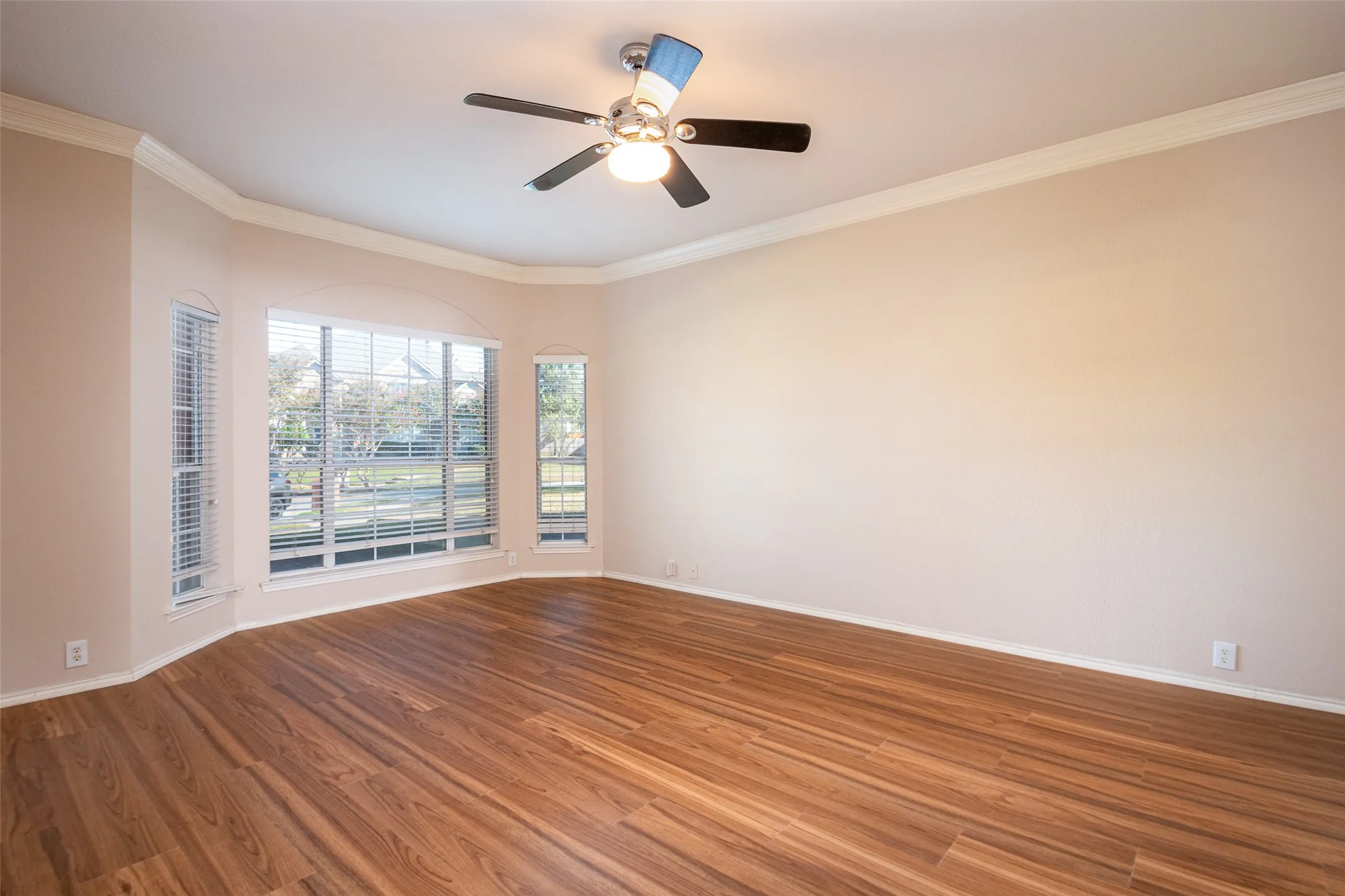 Expansive room featuring wood-finish flooring, a bay window with blinds, and ceiling fan