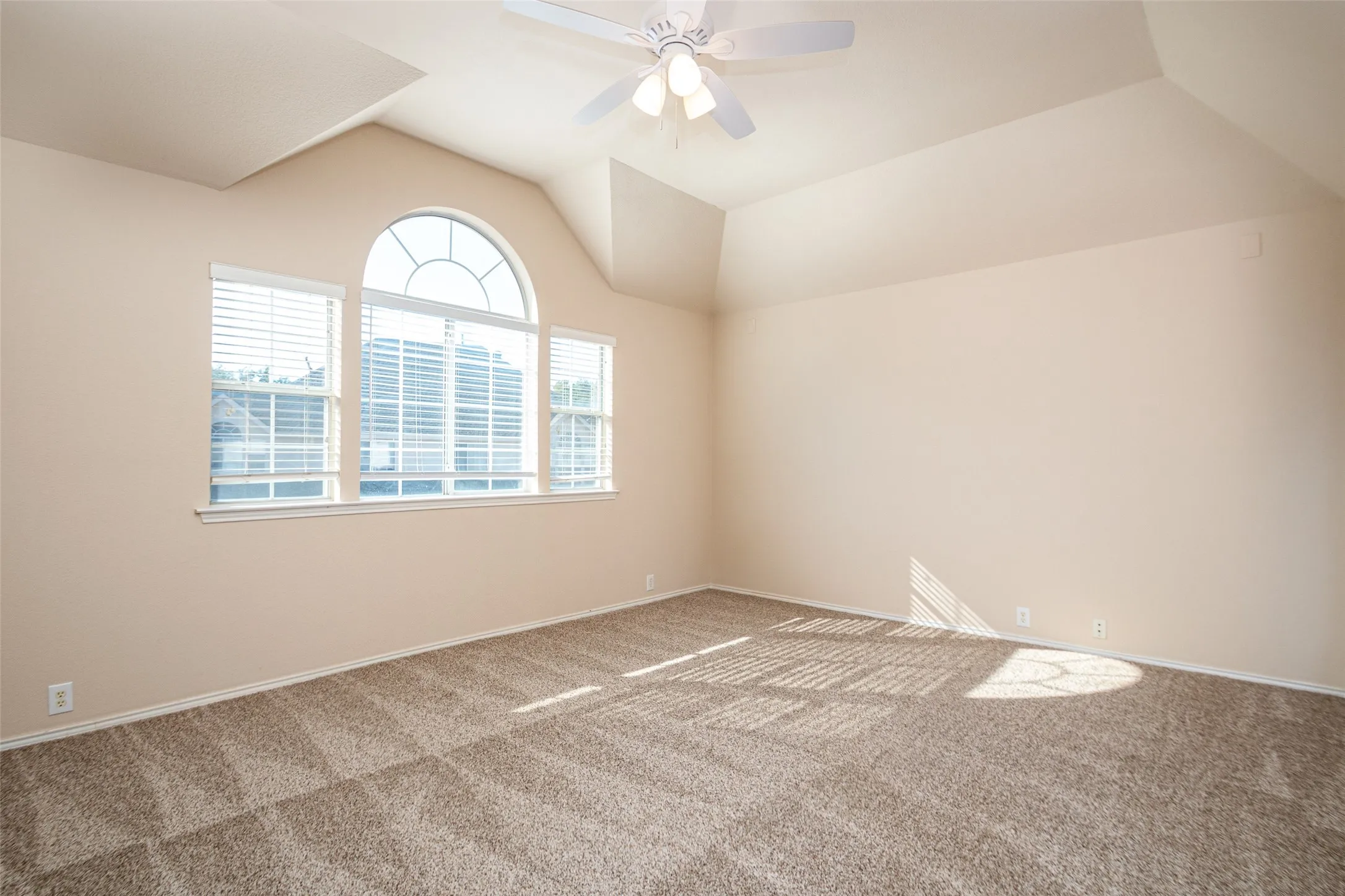 Vaulted ceiling with an arched window, multiple windows with blinds, and a ceiling fan
