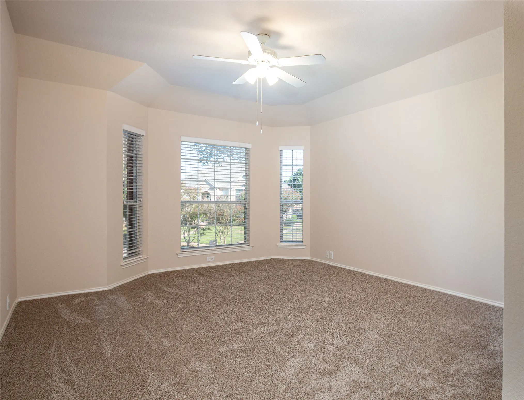 Tray ceiling with a ceiling fan, bay windows with blinds, and wall-to-wall carpeting