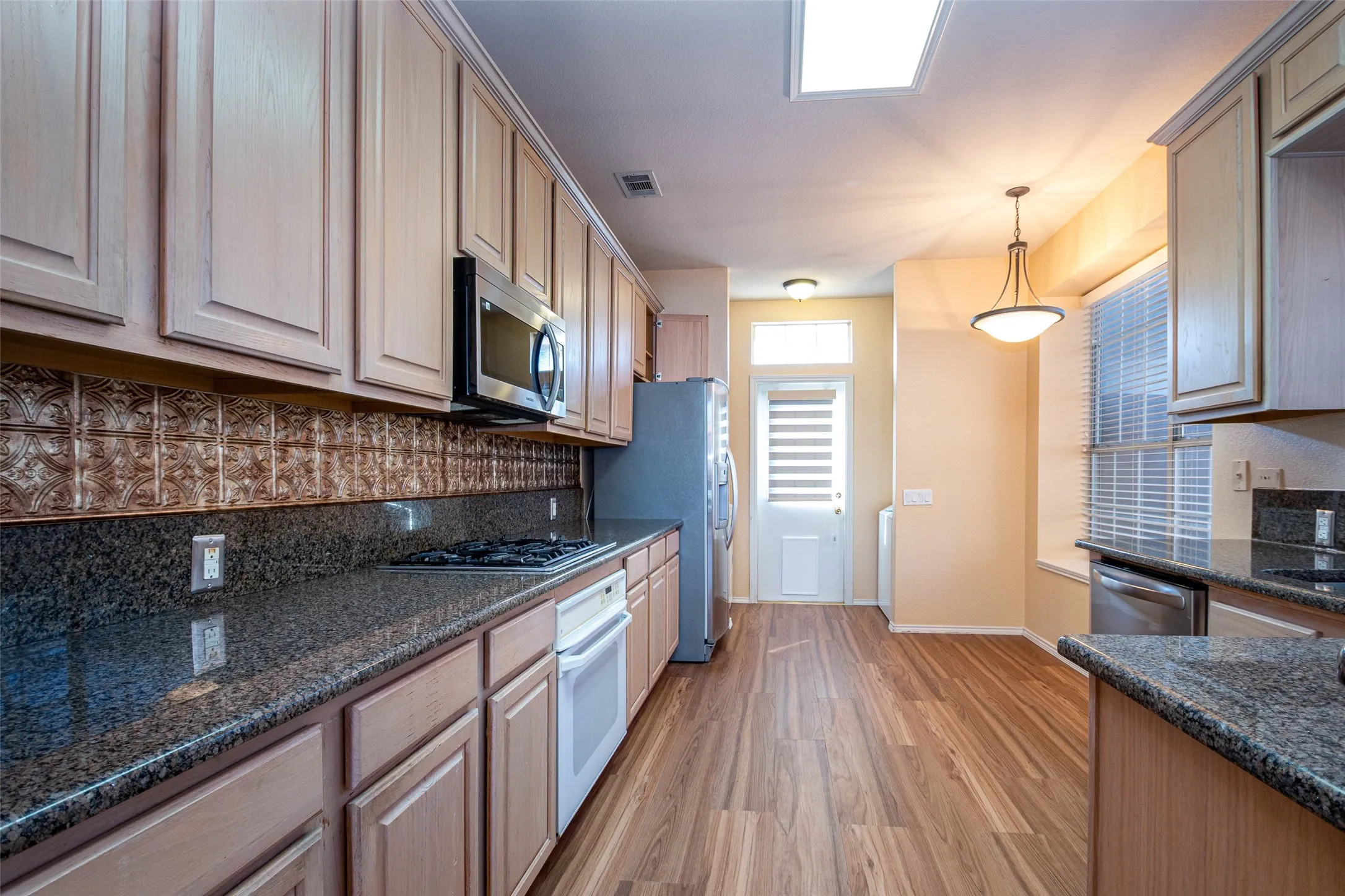 Wood-finish flooring, dark stone countertops, decorative tile backsplash, recessed lighting, and a pendant light fixture