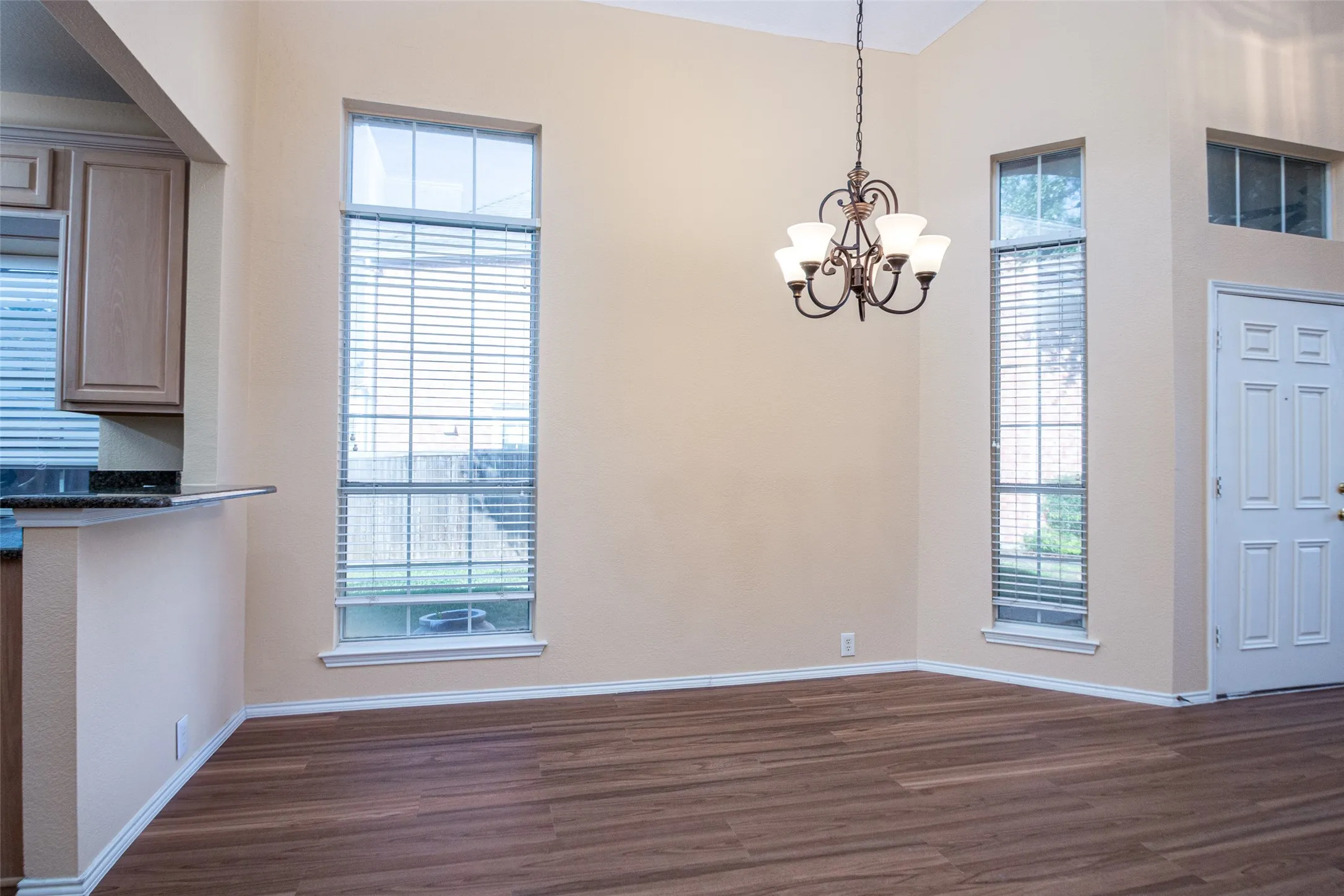 Vaulted ceiling with an iron chandelier, wood-finish flooring, and multiple tall windows