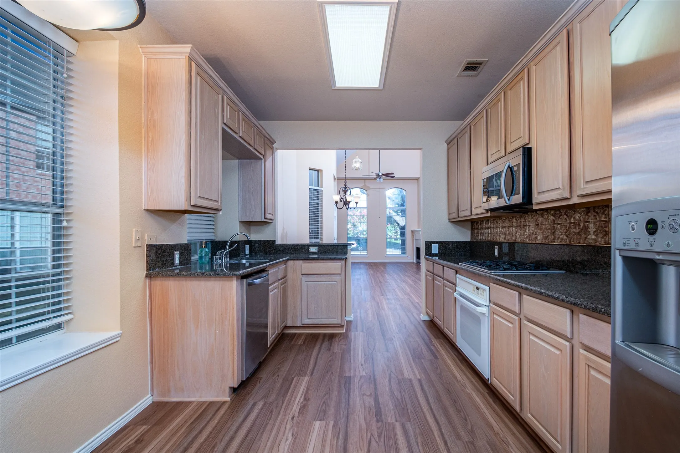 Galley-style kitchen featuring wood-finish flooring, wood cabinetry, dark countertops, and stainless steel appliances