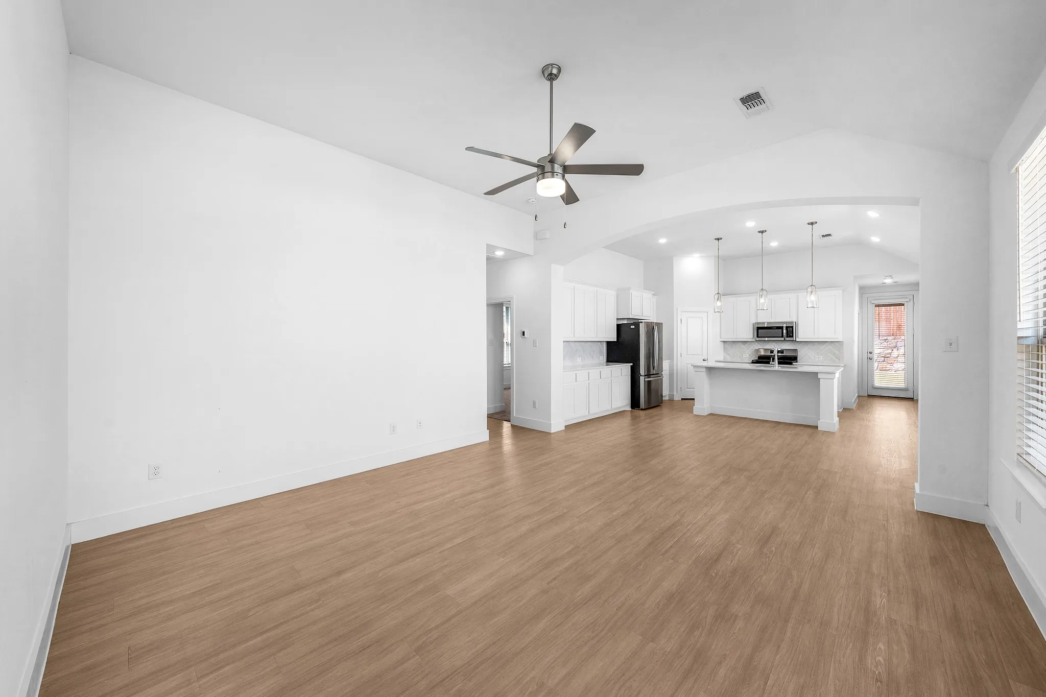 Open concept living space with vaulted ceilings, wood-finish flooring, and a ceiling fan