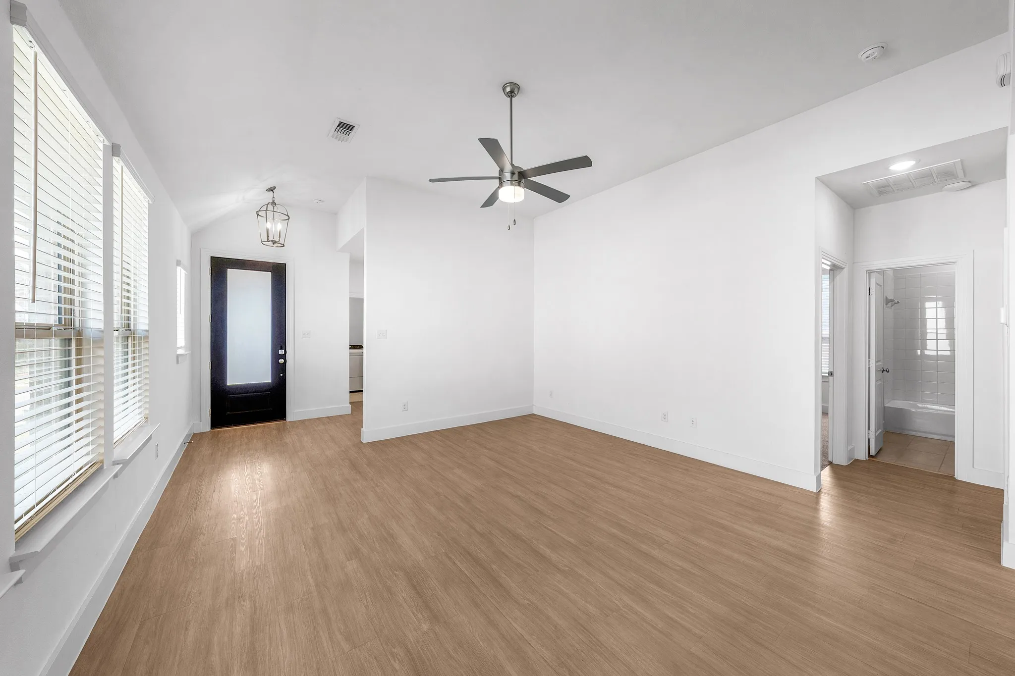 Spacious room featuring wood-finish flooring, a modern ceiling fan, and multiple windows with blinds