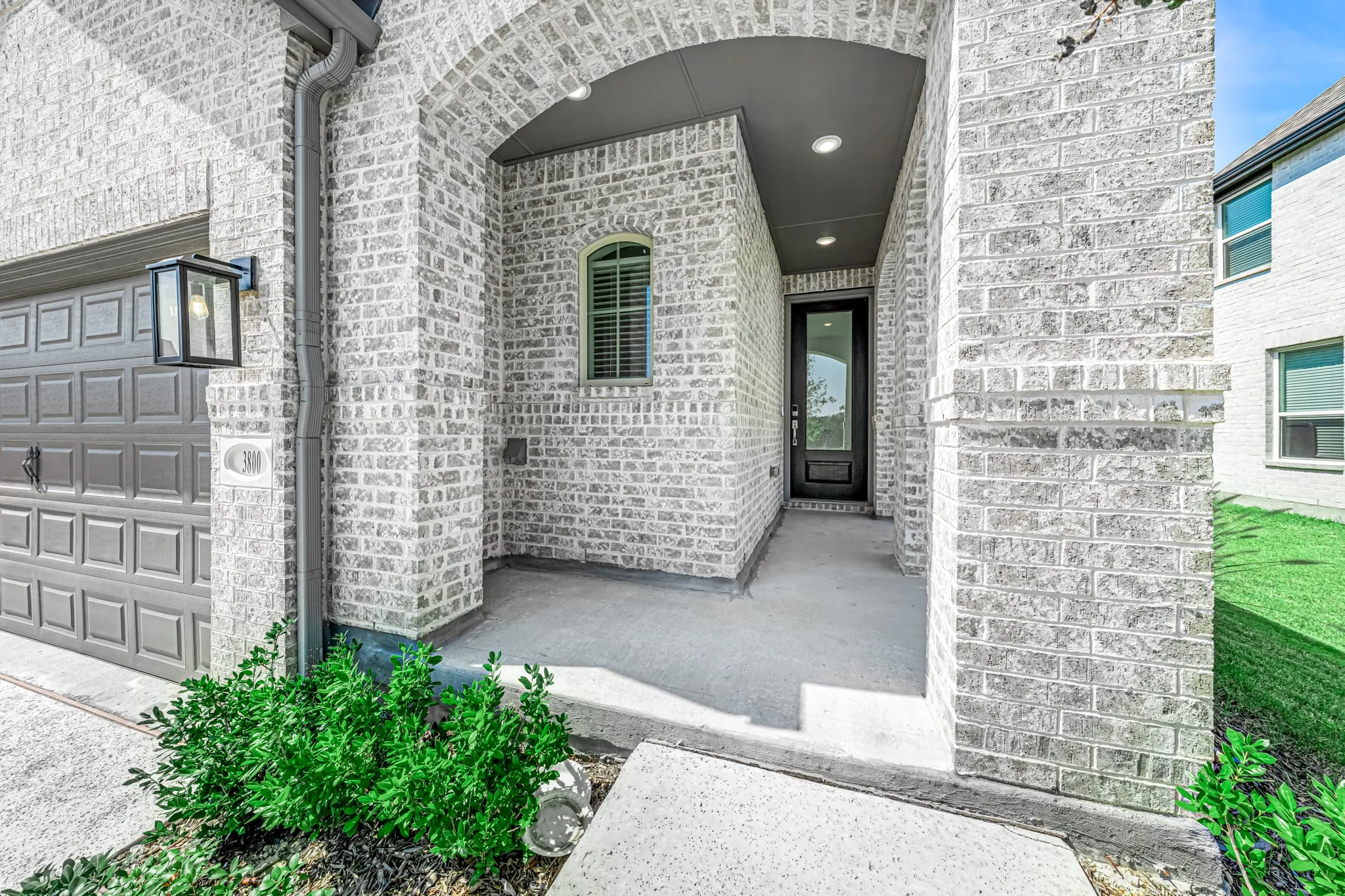 Light brick exterior with an arched entryway, recessed lighting, and a dark paneled garage door