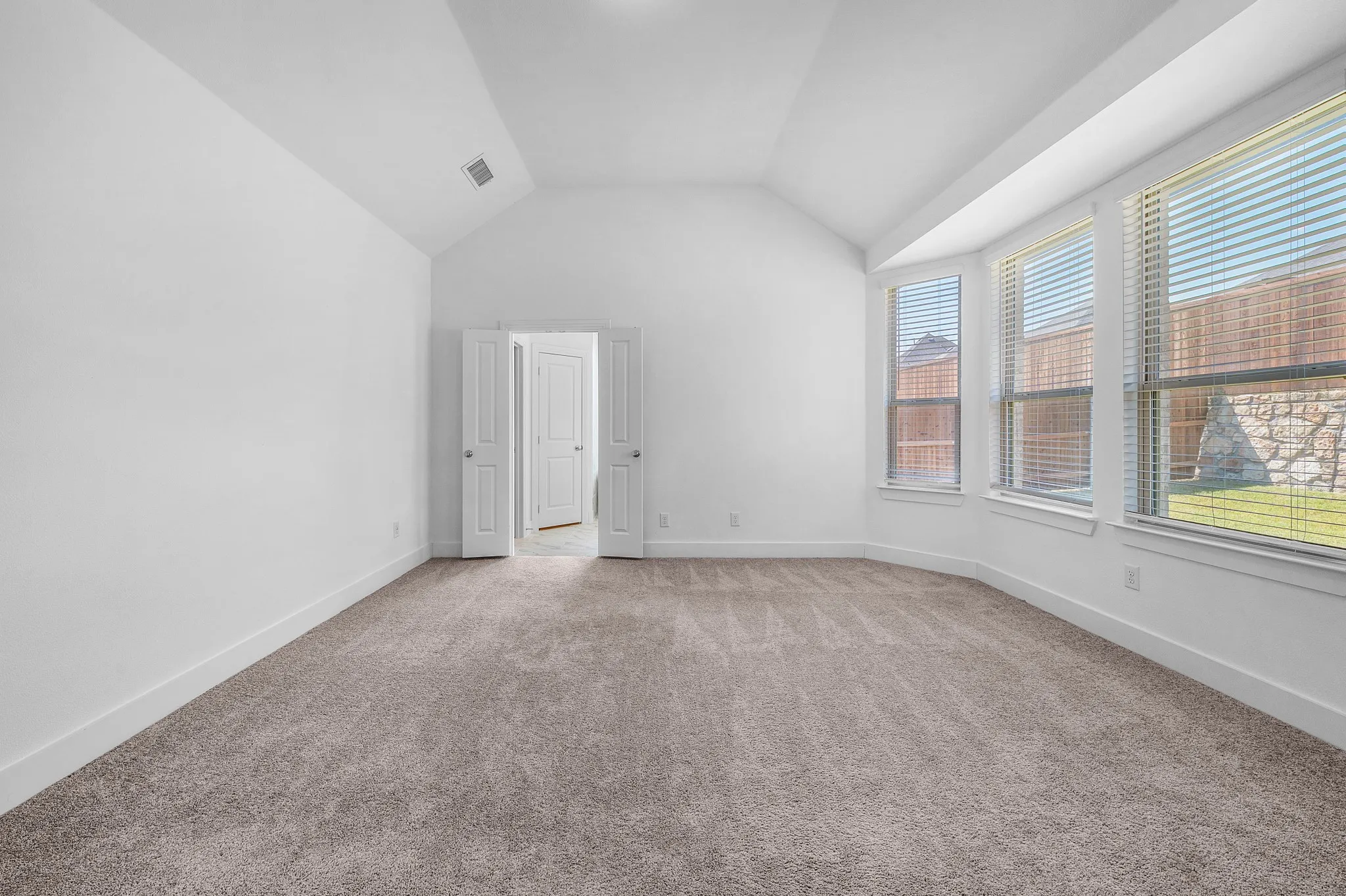 Vaulted ceiling, carpeted flooring, white walls, multiple windows with blinds, and white trim throughout