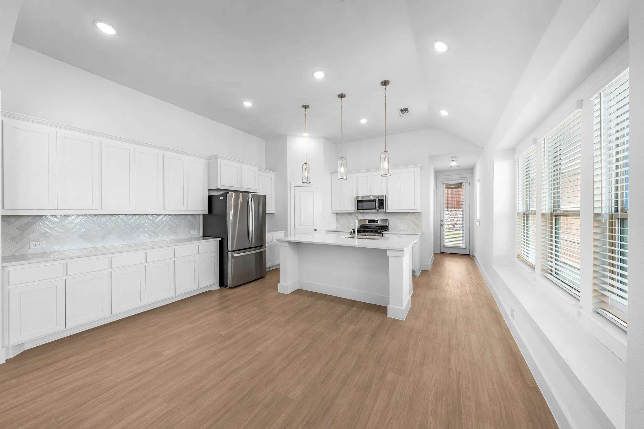 Open-concept kitchen with white cabinetry, stainless steel appliances, and wood-finish flooring