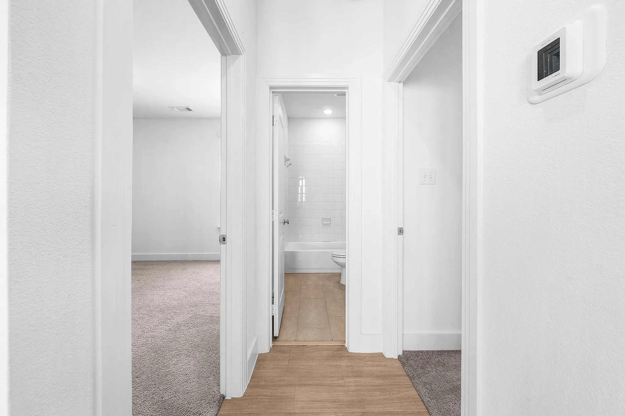 Wood-finish flooring, white subway tile shower surround, and a neutral carpeted room