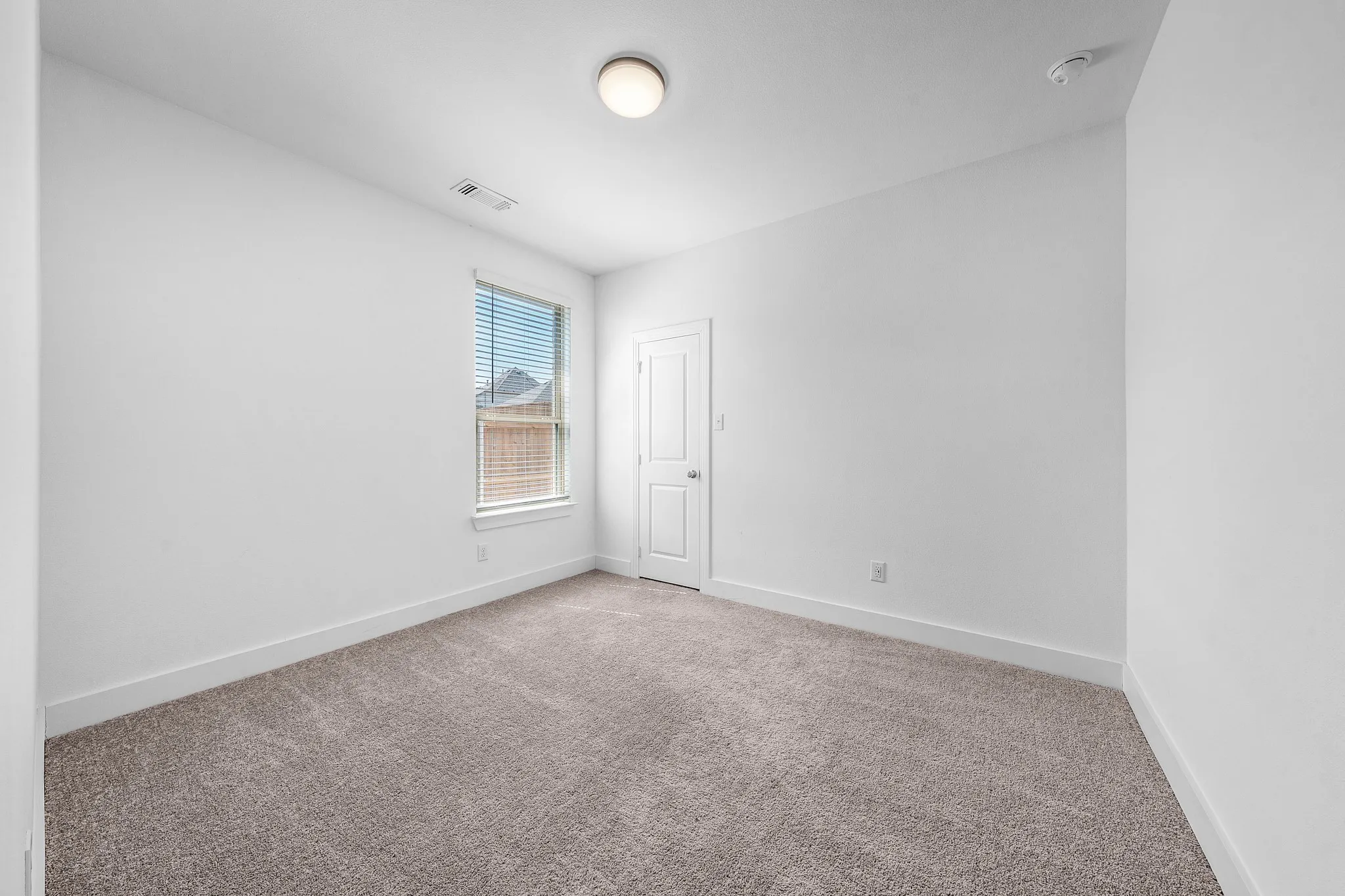 Neutral tone wall paint, carpet flooring, window with blinds, flush mount ceiling light, and interior door
