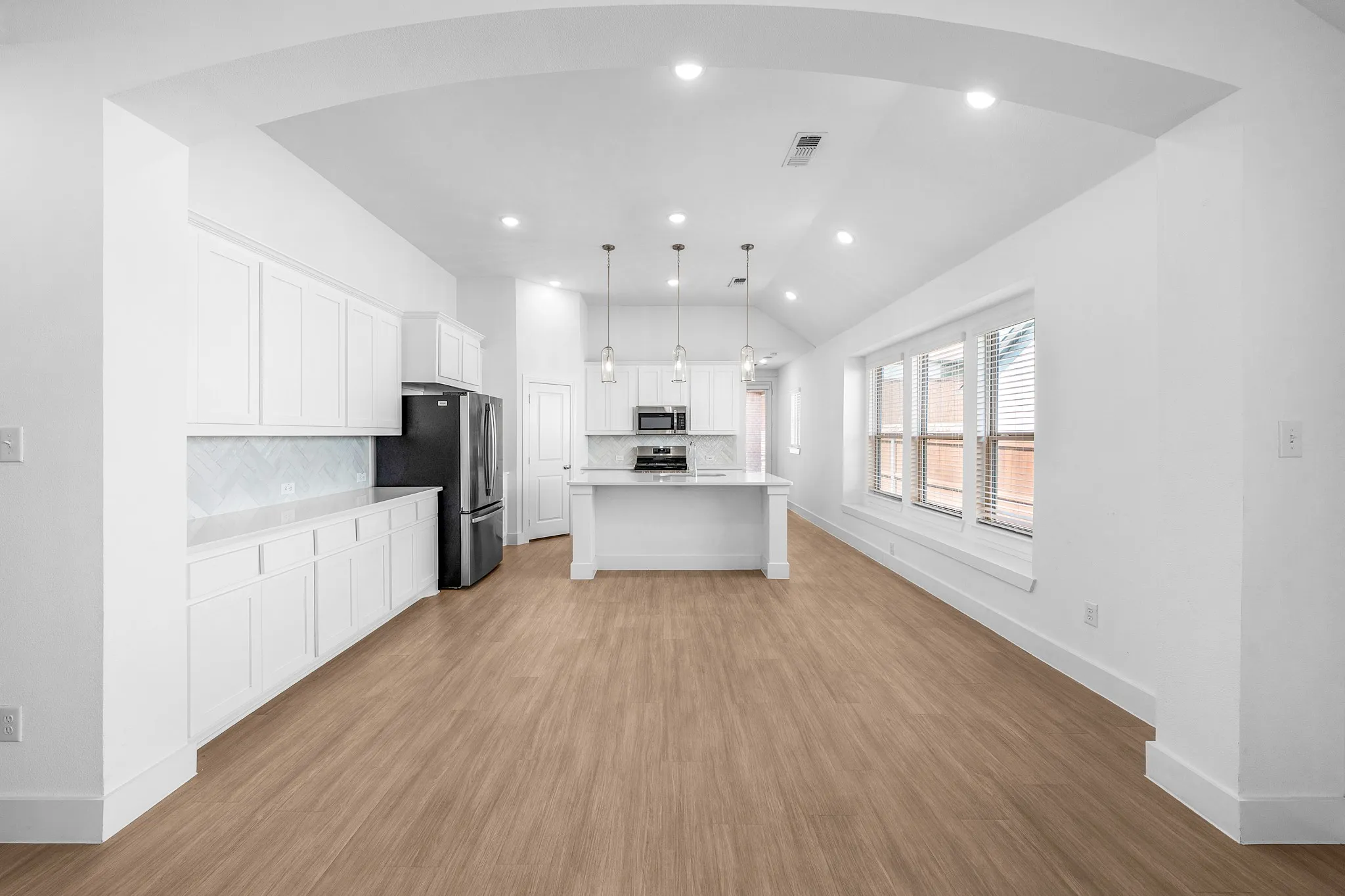Open-concept living area with wood-finish flooring, white cabinetry, a kitchen island, and recessed lighting