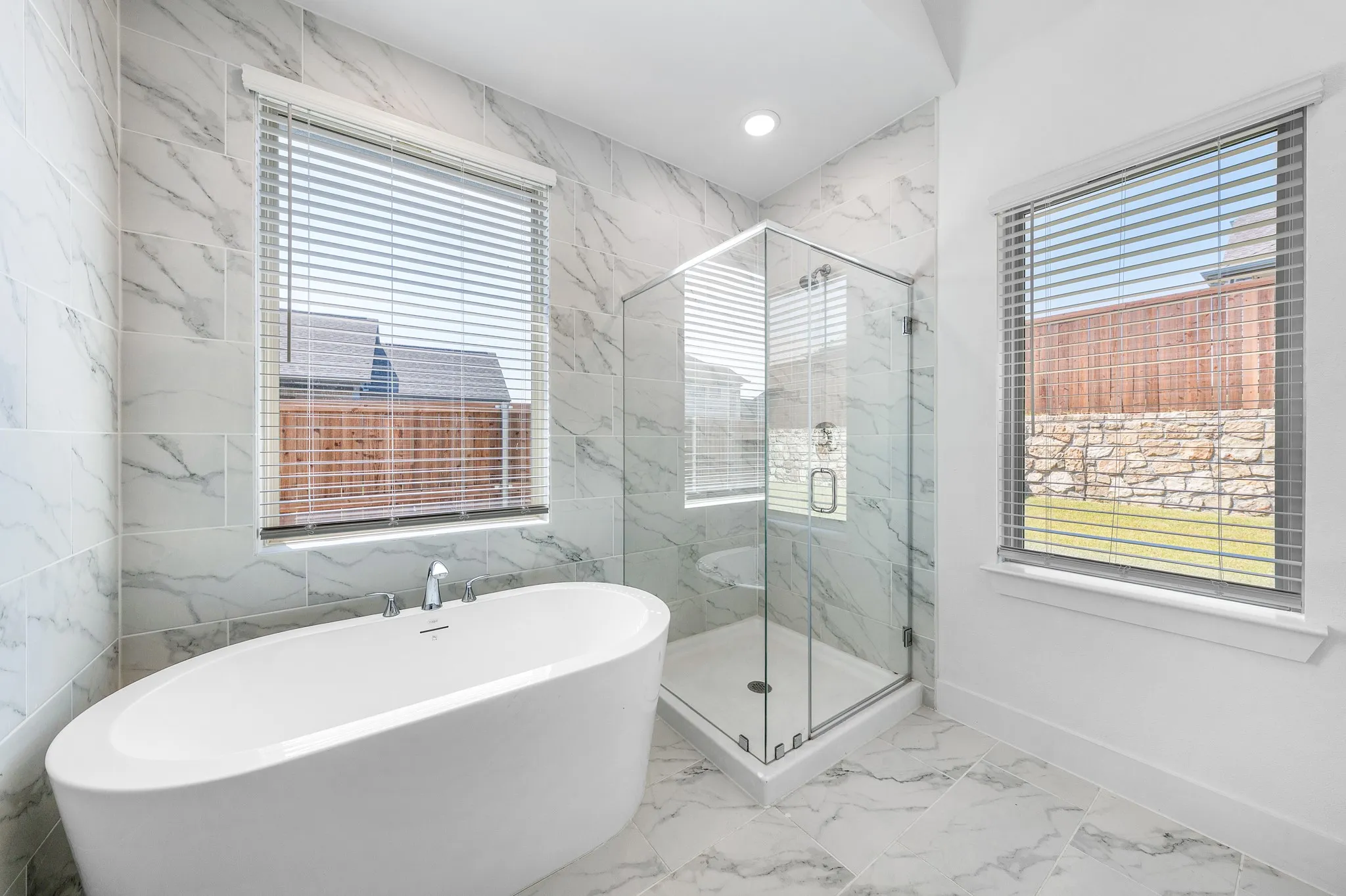 Freestanding oval soaking tub with chrome fixtures, glass-enclosed shower with bench, and large format wall and floor tile