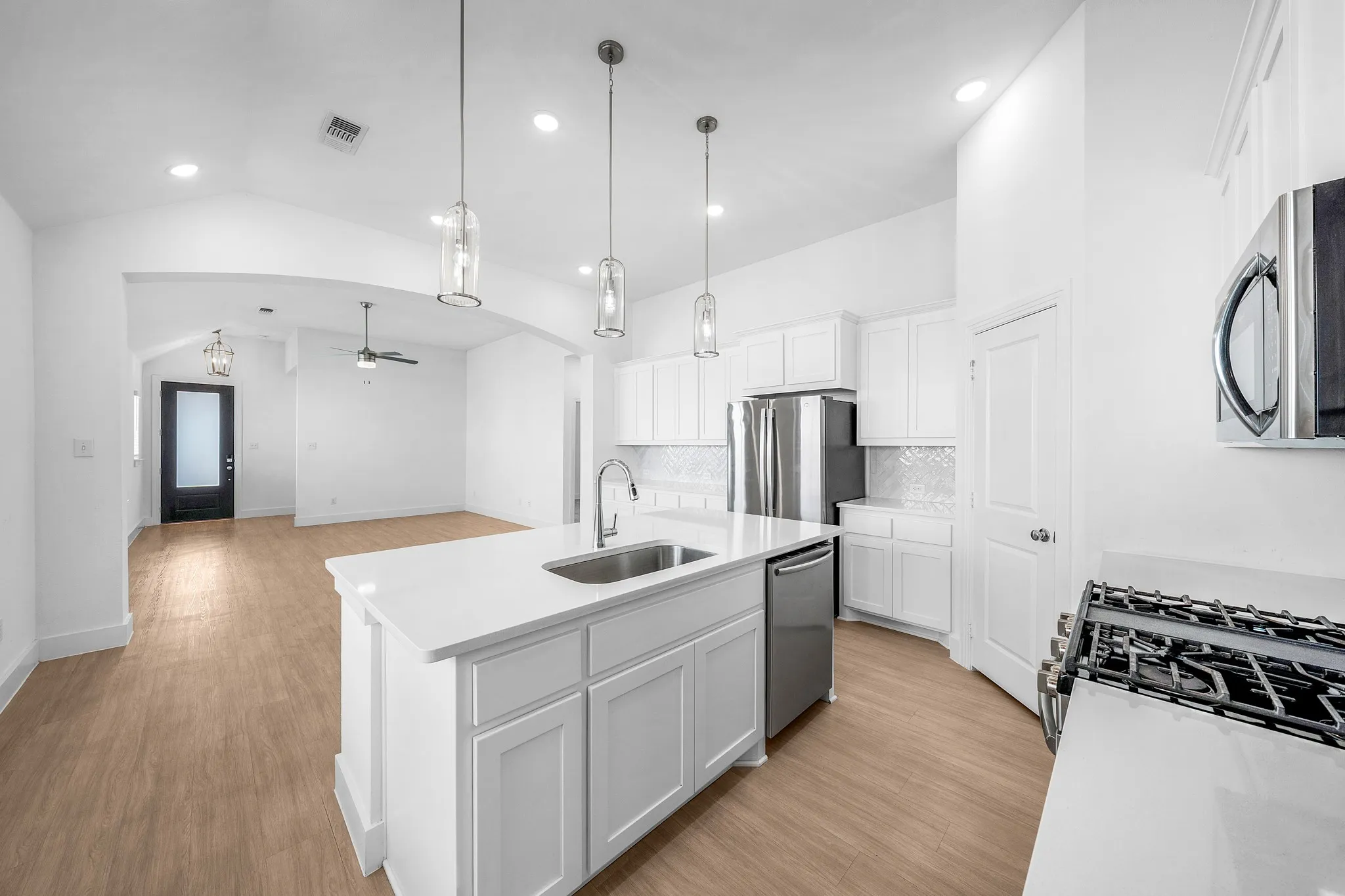 Open-concept kitchen featuring an island with an integrated sink, white cabinetry, stainless steel appliances, and wood-finish flooring