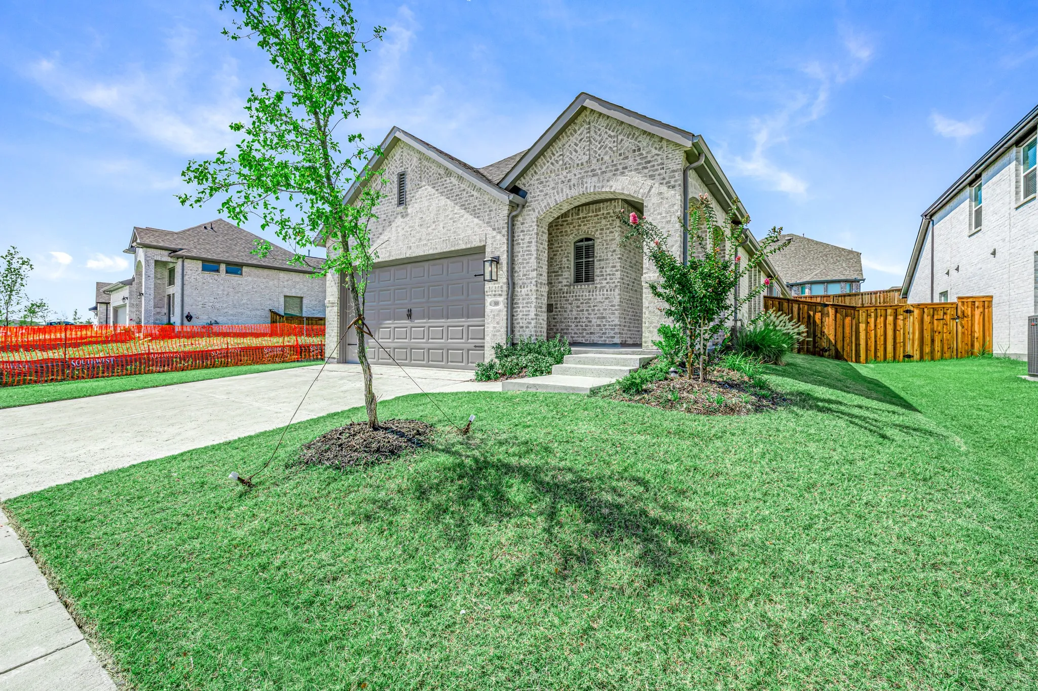 Brick exterior with arched entry, two-car garage, mature landscaping, and privacy fencing