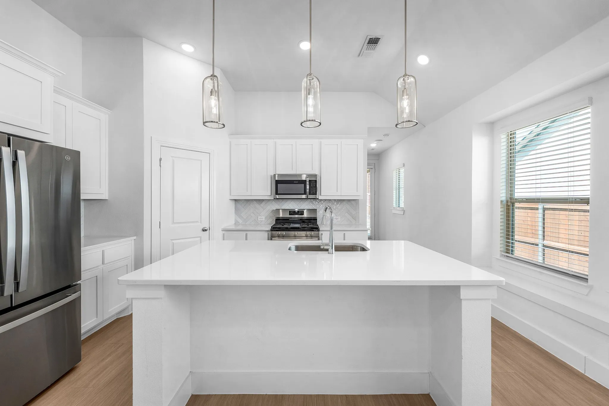 Bright kitchen featuring a center island, recessed lighting, pendant fixtures, stainless steel appliances, and wood-finish flooring