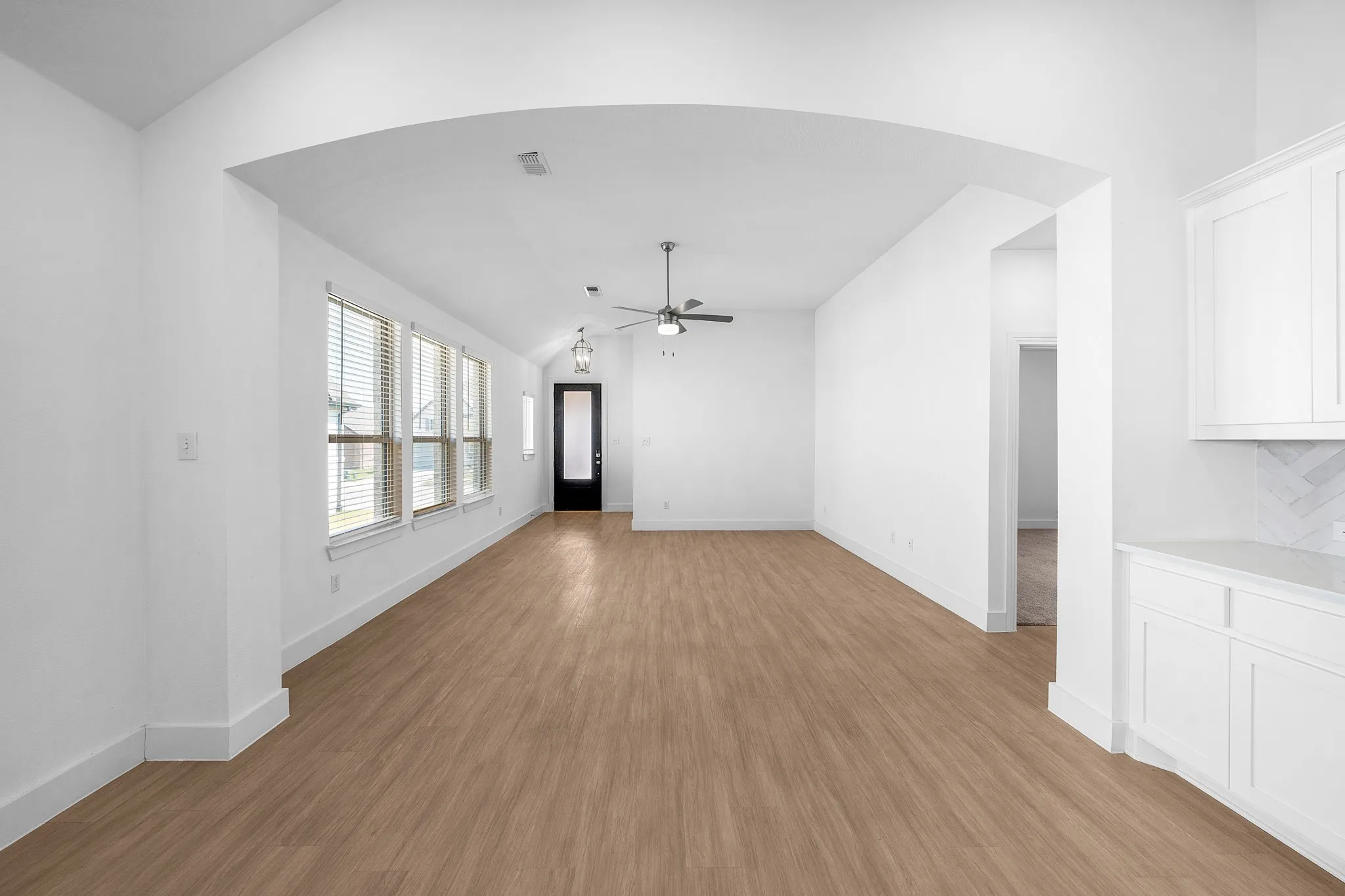 Wood-finish flooring, recessed lighting, white cabinetry with stone countertops, and a full wall of windows with blinds