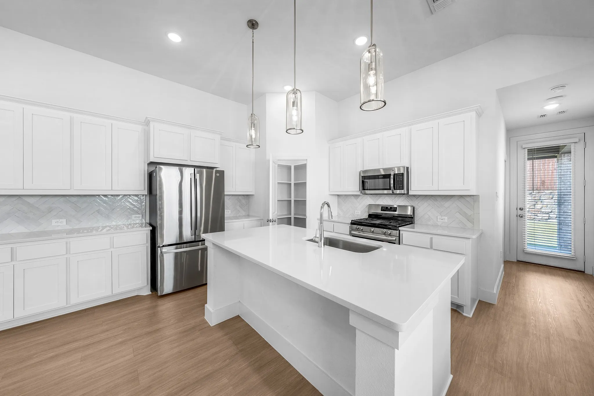 White cabinetry with brushed nickel hardware, stainless steel appliances, herringbone tile backsplash, and wood-finish flooring