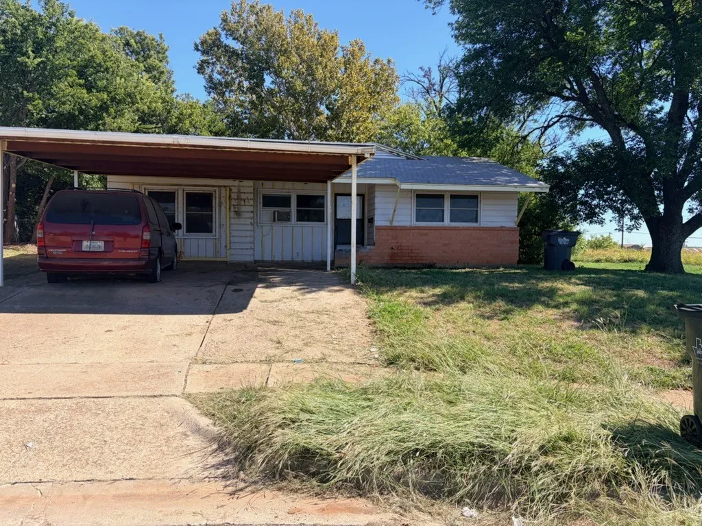 Carport with concrete driveway, mature trees, and brick detailing on the facade