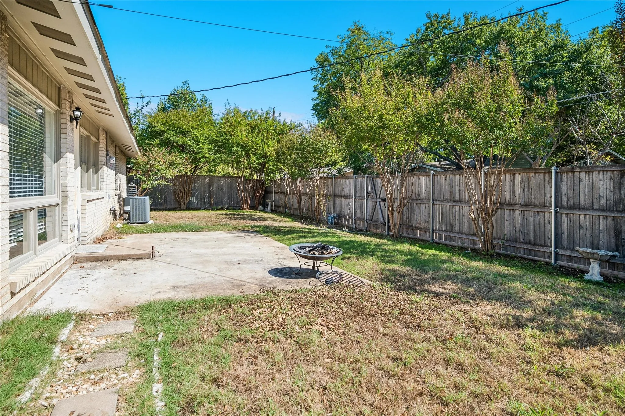 Expansive backyard featuring a privacy fence, mature trees, concrete patio, and exterior brick siding