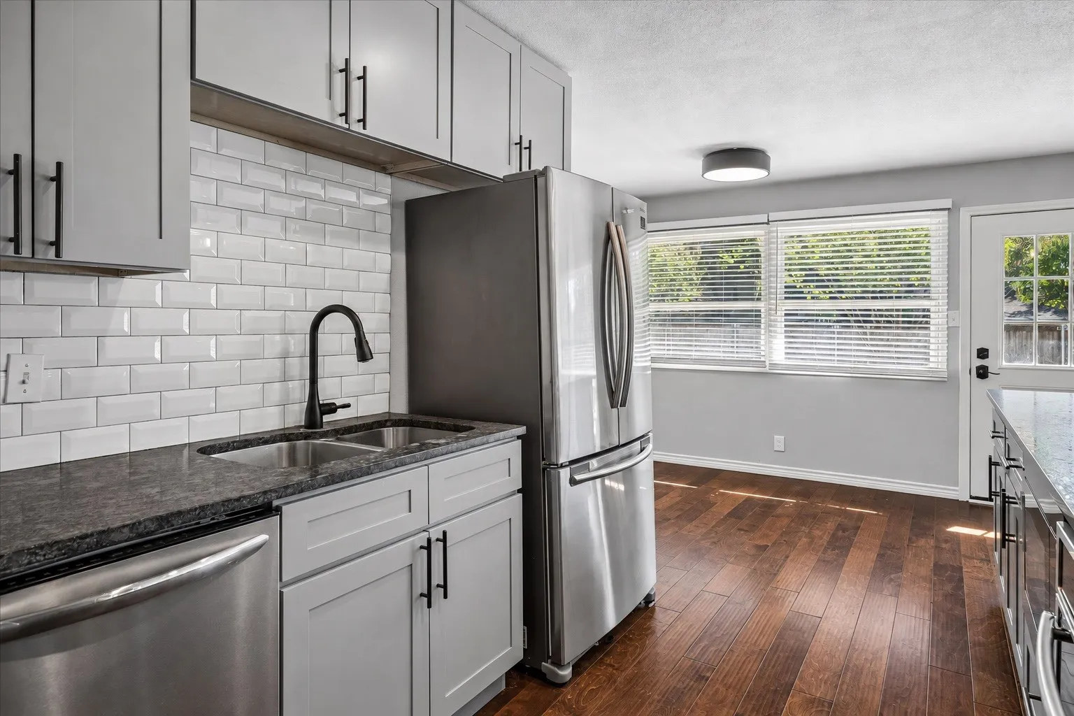 Kitchen featuring light gray cabinetry, stainless steel appliances, dark stone-finish countertops, and wood-finish flooring