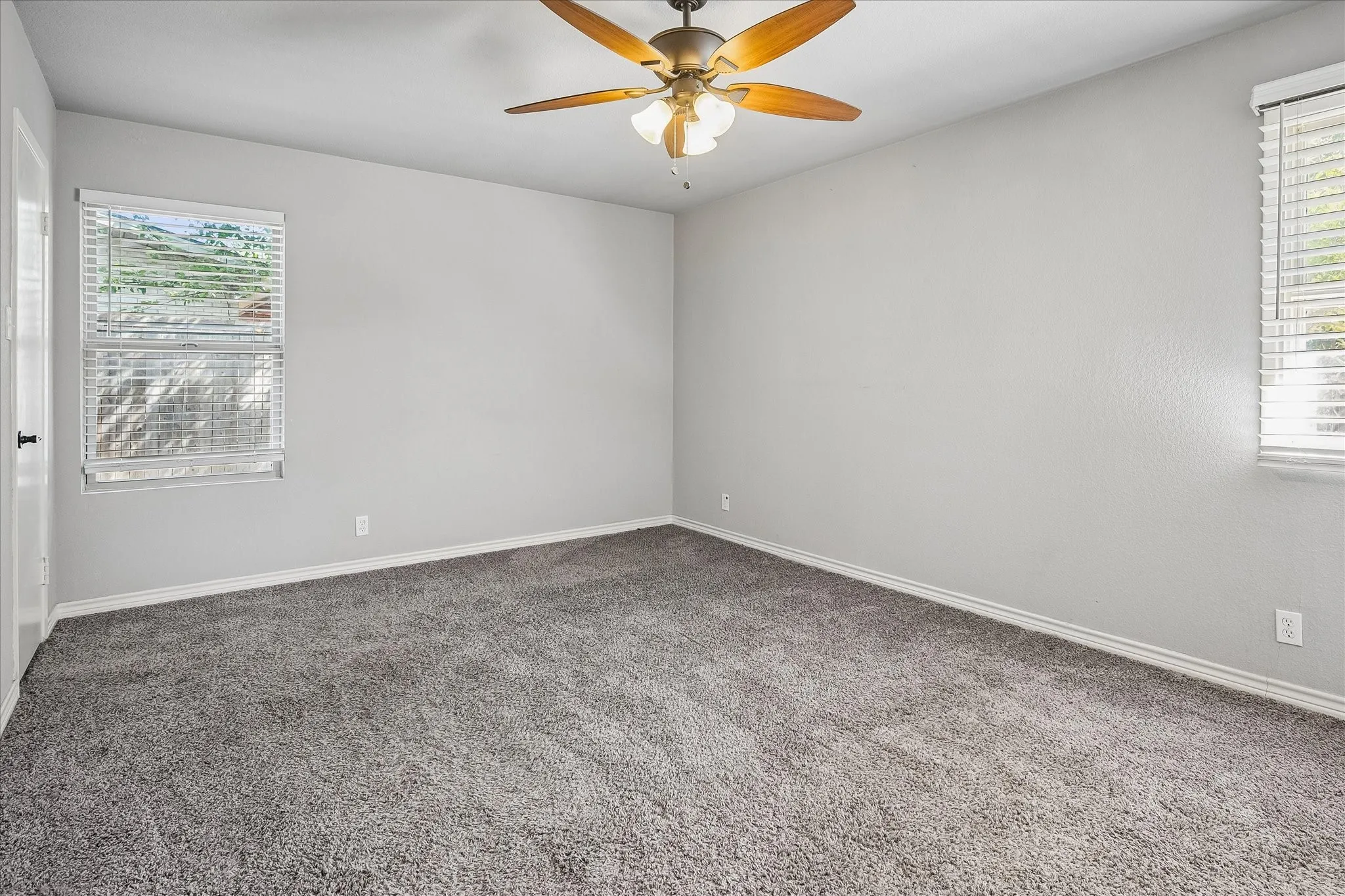 Room featuring gray textured carpeting, neutral wall paint, and two windows with blinds